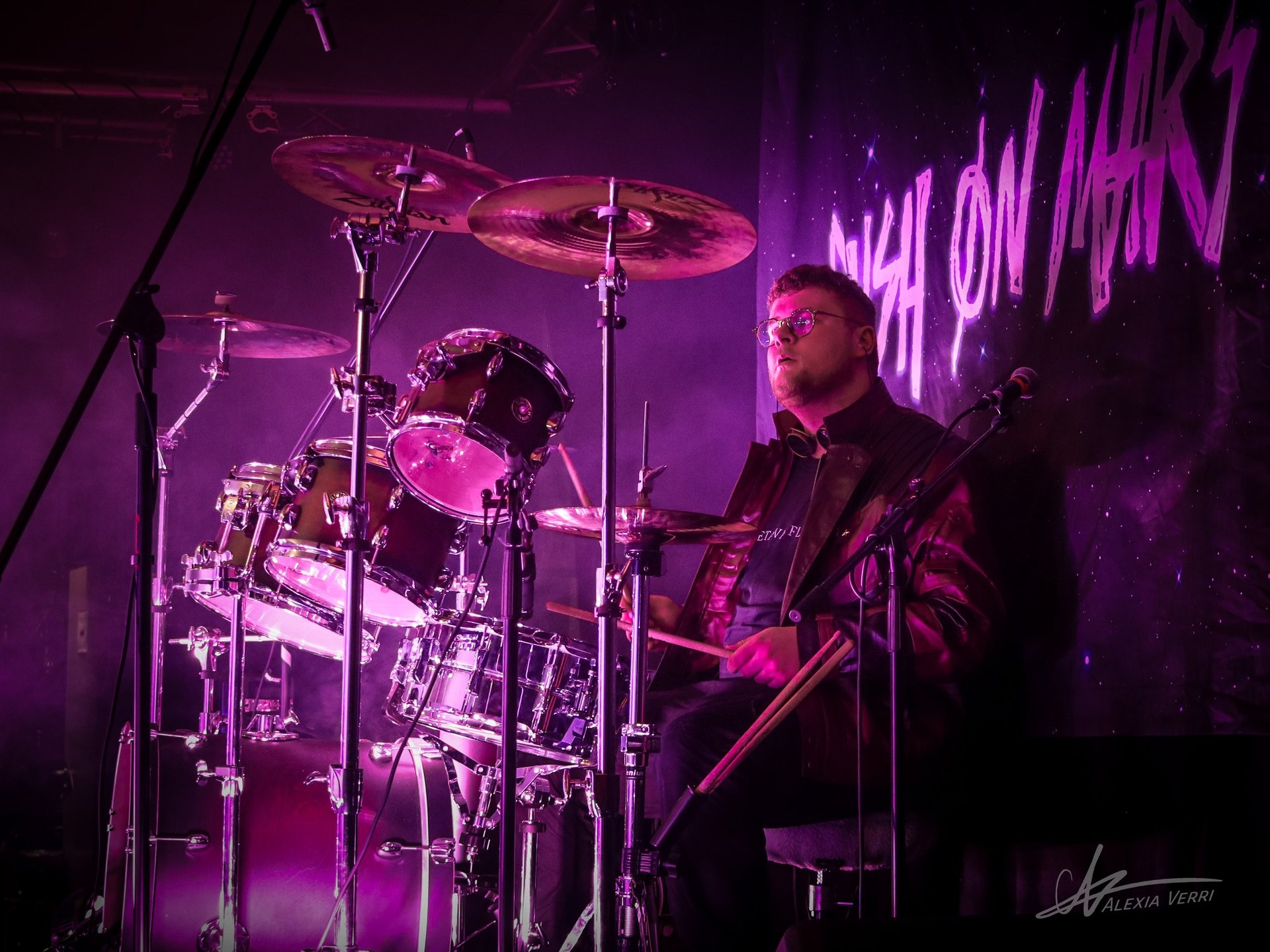  arthur debary le batteur jouant de la batterie lors du faster than light festival illuminé d'un spot rose, devant notre logo