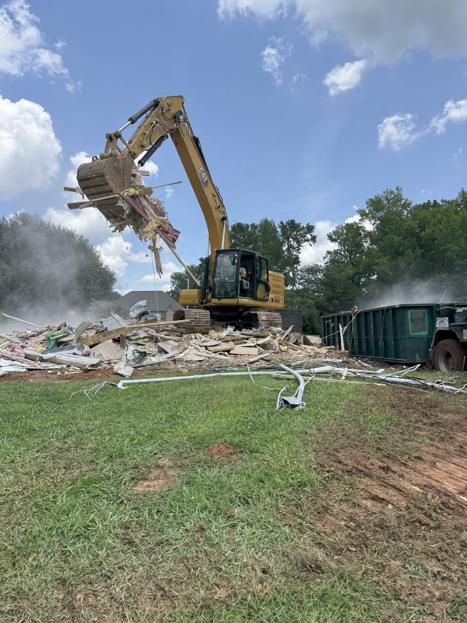 Excavator loading demolition debris in dumpster