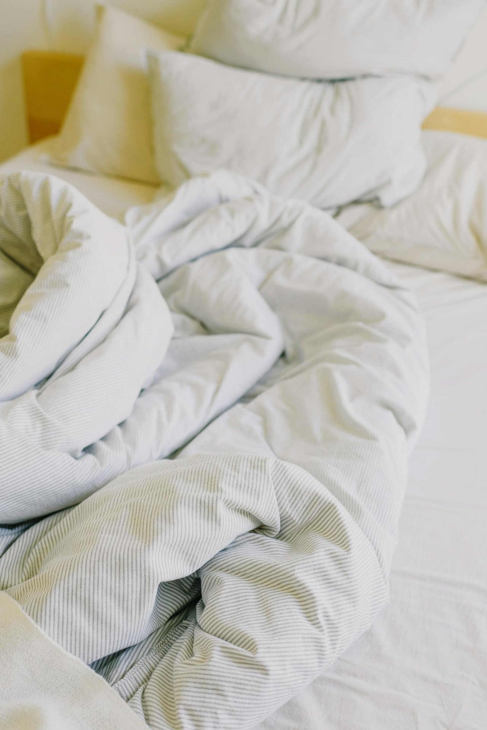 an unmade bed with white sheets, pillows and cover