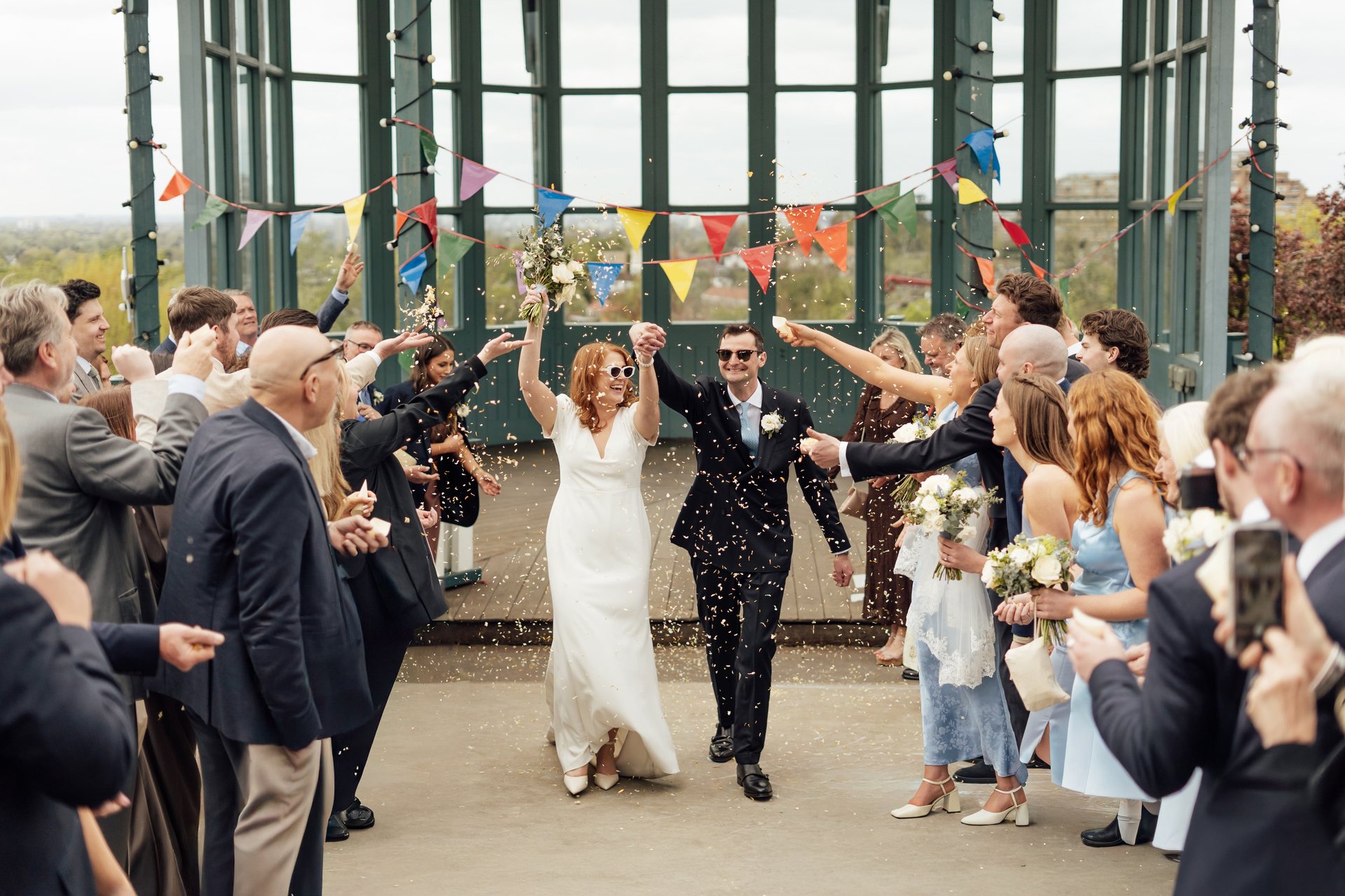Bride and groom walking through confetti time and laughing with their hands up