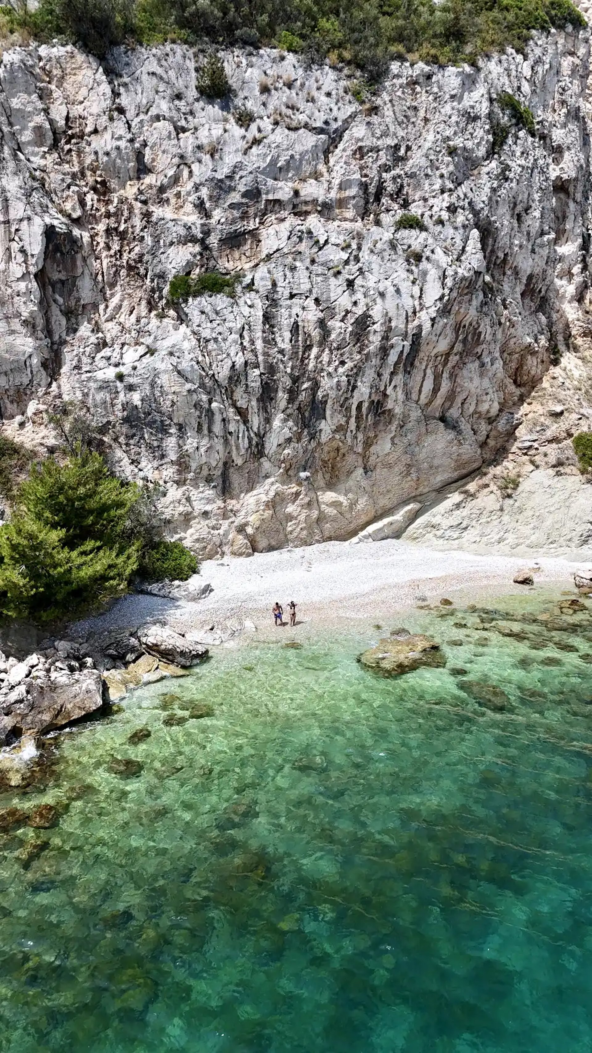 Aerial panoramic view of a hidden beach, a couple and dramatic cliffs on Ciovo during a private boat tour from Split, Croatia