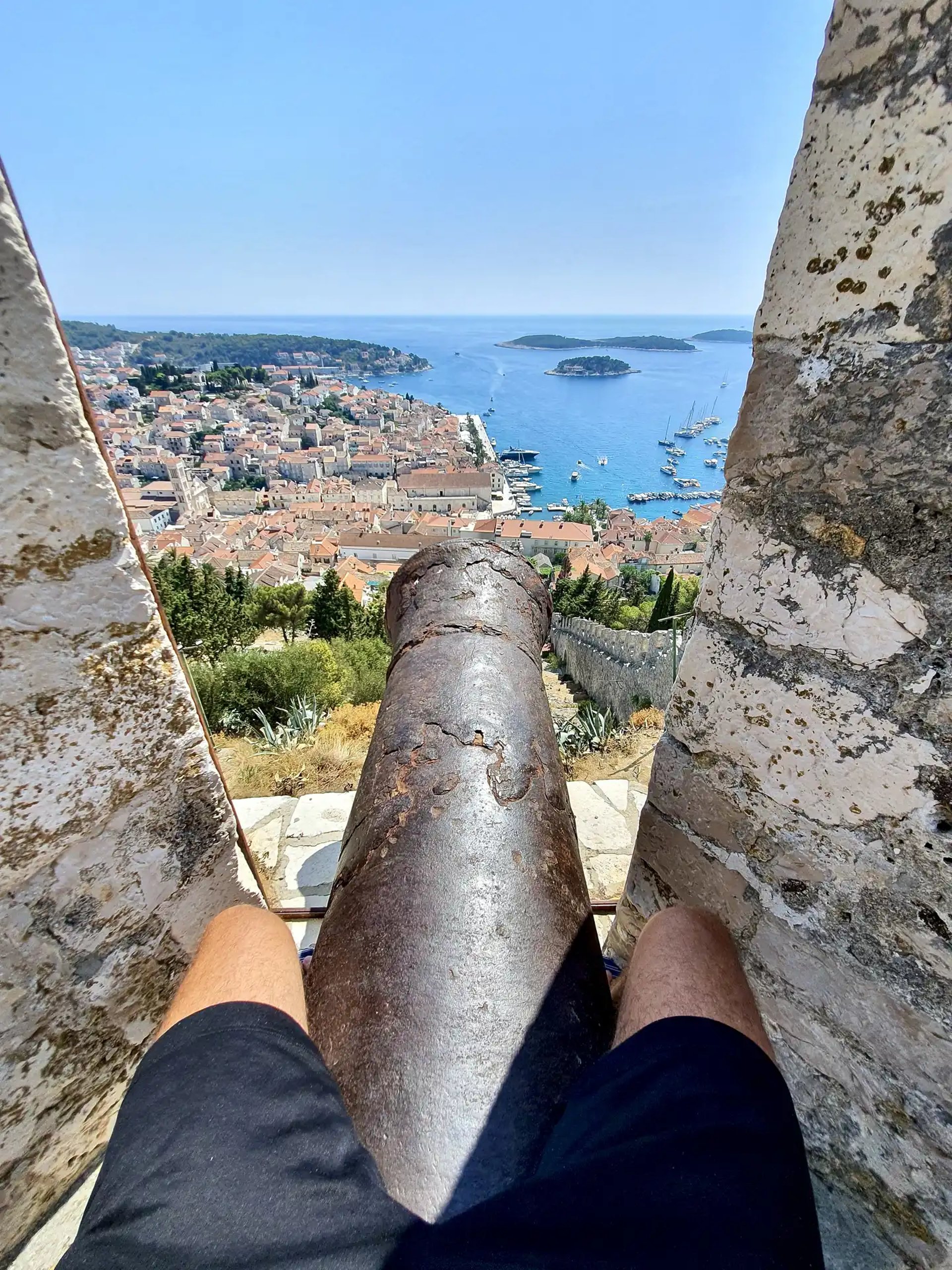 Panoramic view of Hvar town and Pakleni Islands from Fortica Fortress with a man sitting on a cannon during boat tour