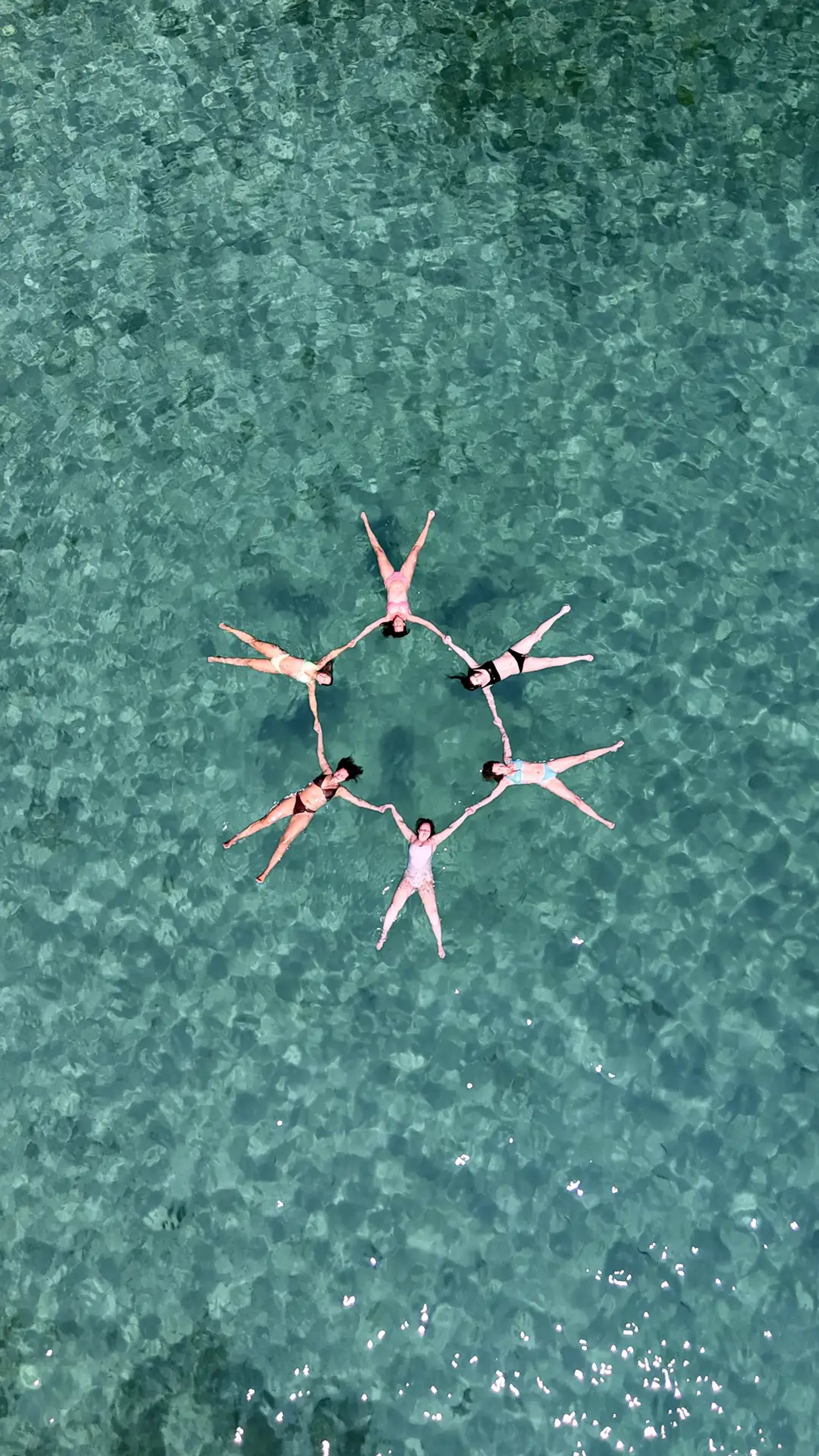 Drone view of girls forming a star while floating in crystal-clear waters of Drvenik Mali on a private boat tour from Split