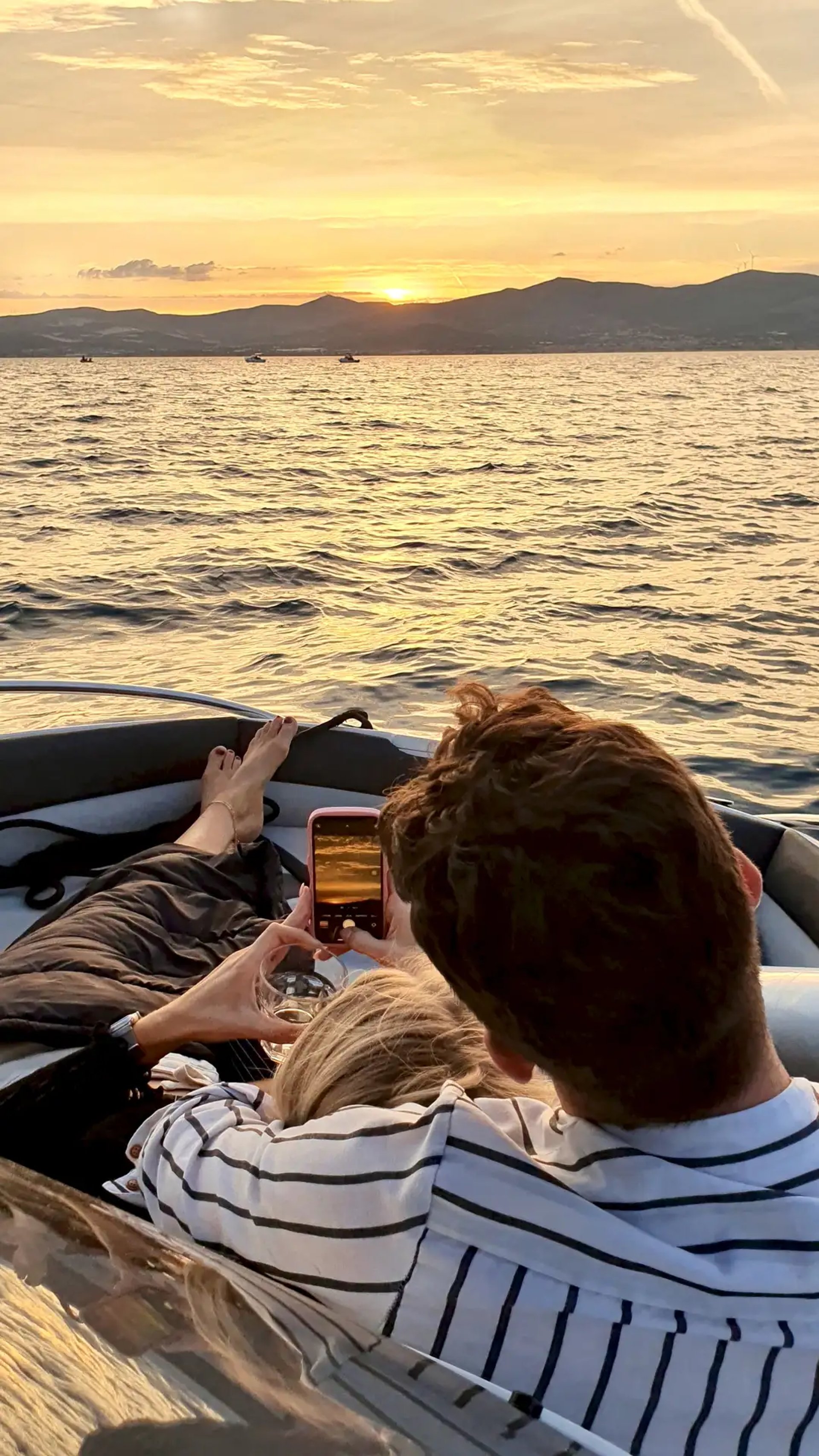 Couple hugging while the woman photographs the sunset during a romantic sunset cruise from Split