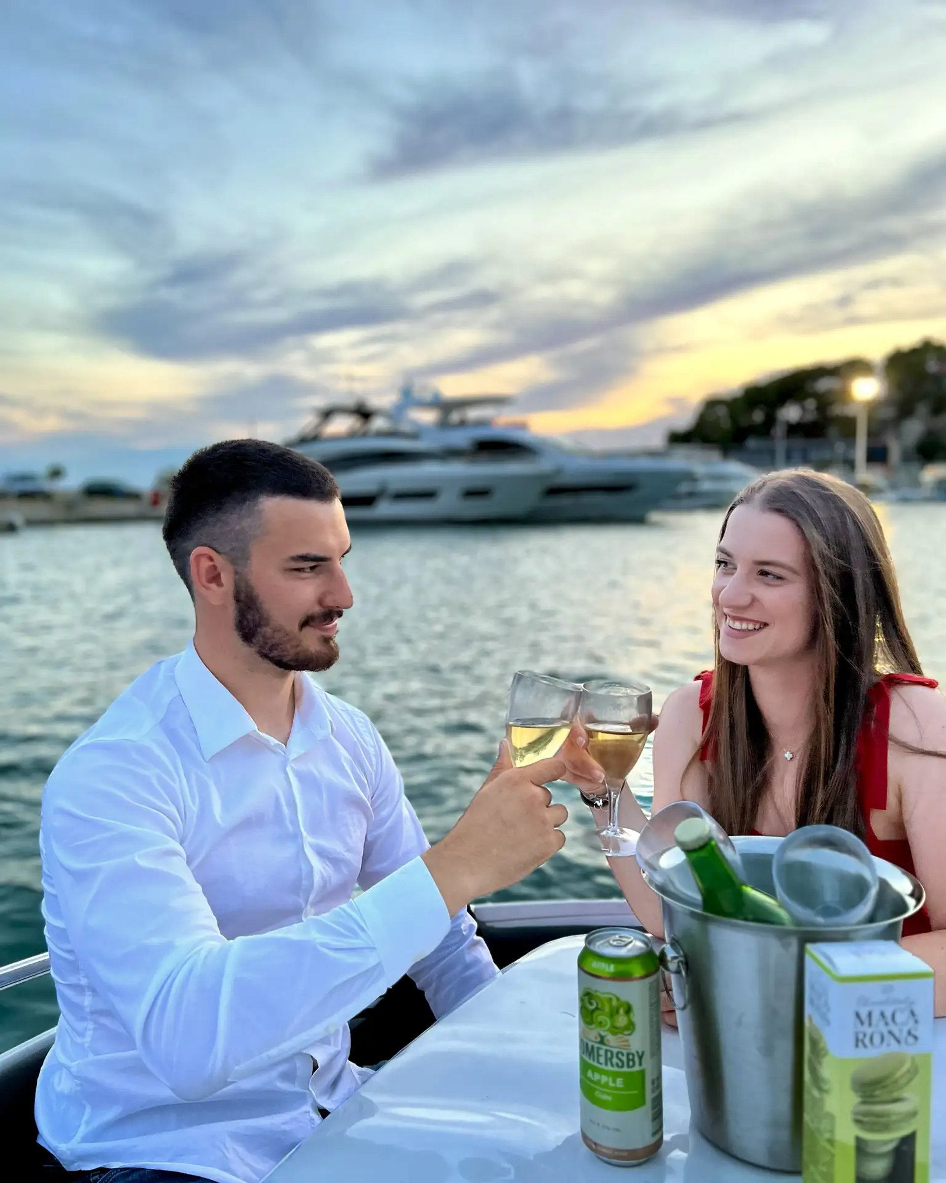 Couple smiling looking at each other toasting drinks on the bow table of a speedboat during a romantic sunset tour from Split