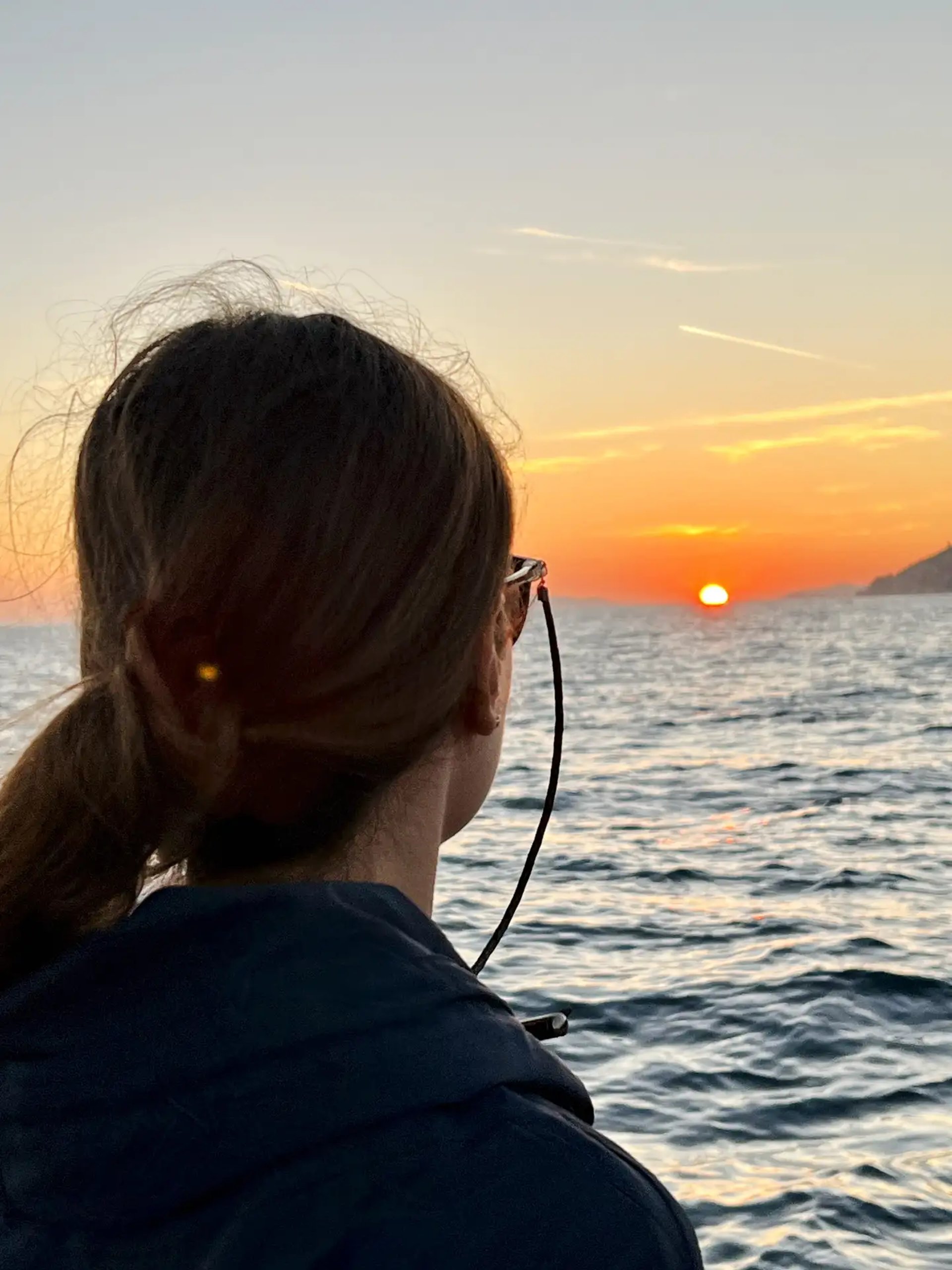 Female guest watching the sun touch the Adriatic horizon during a sunset cruise from Split