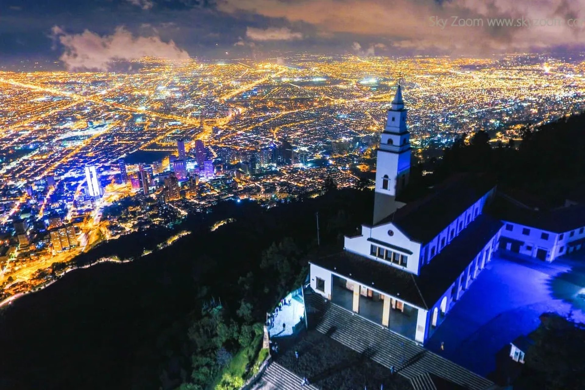 The illuminated Monserrate church at night overlooking the glowing Bogota city lights on a private tour