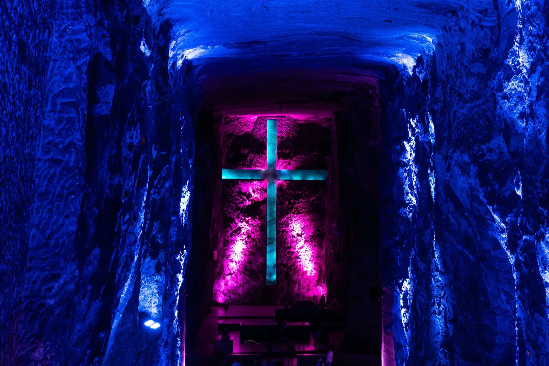 Dramatic view of the giant rock-carved cross illuminated by purple lights inside Zipaquira Salt Cathedral.