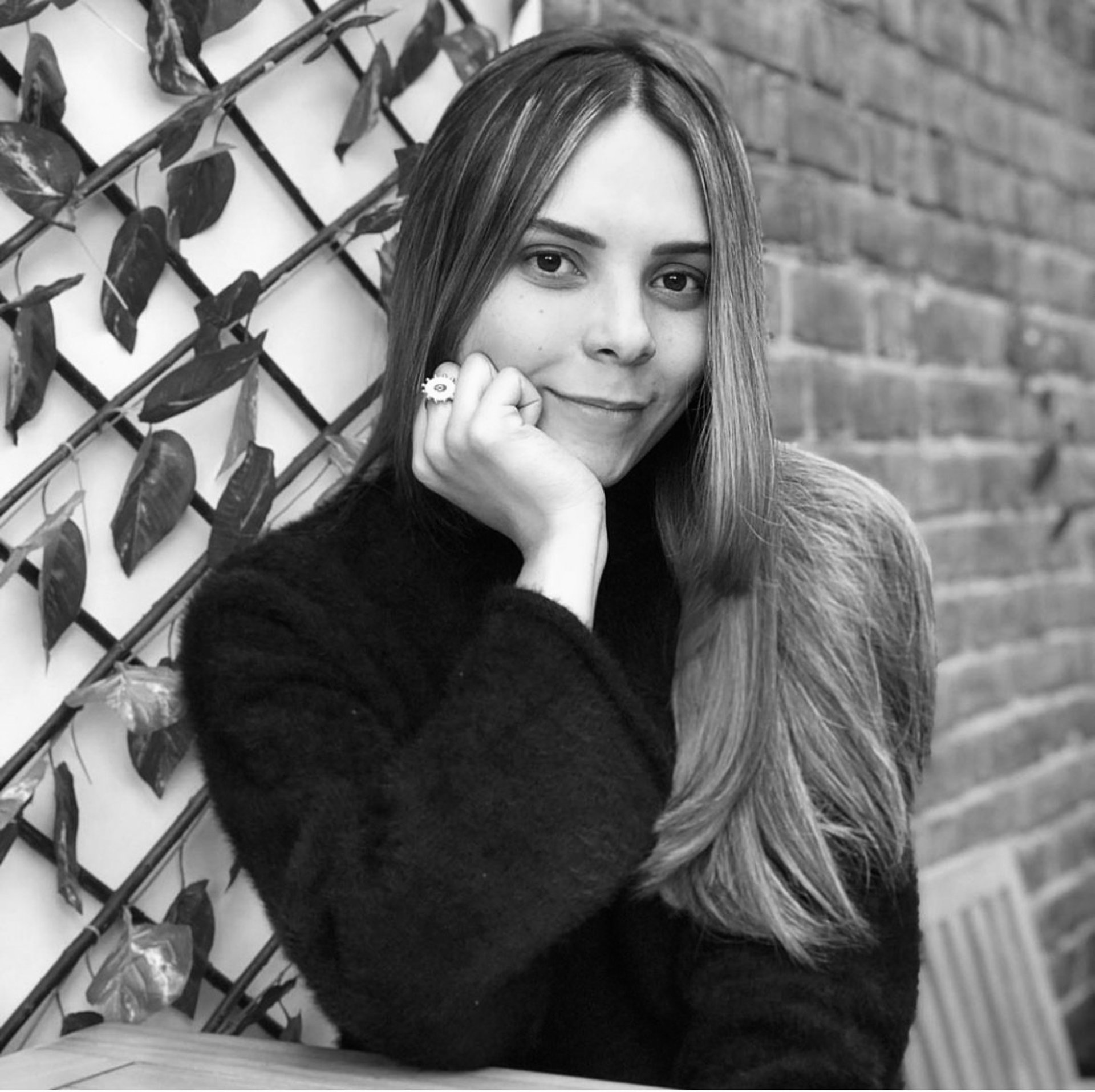 una mujer sonriendo a la camara sutilmente con su mano sosteniendo su cara
