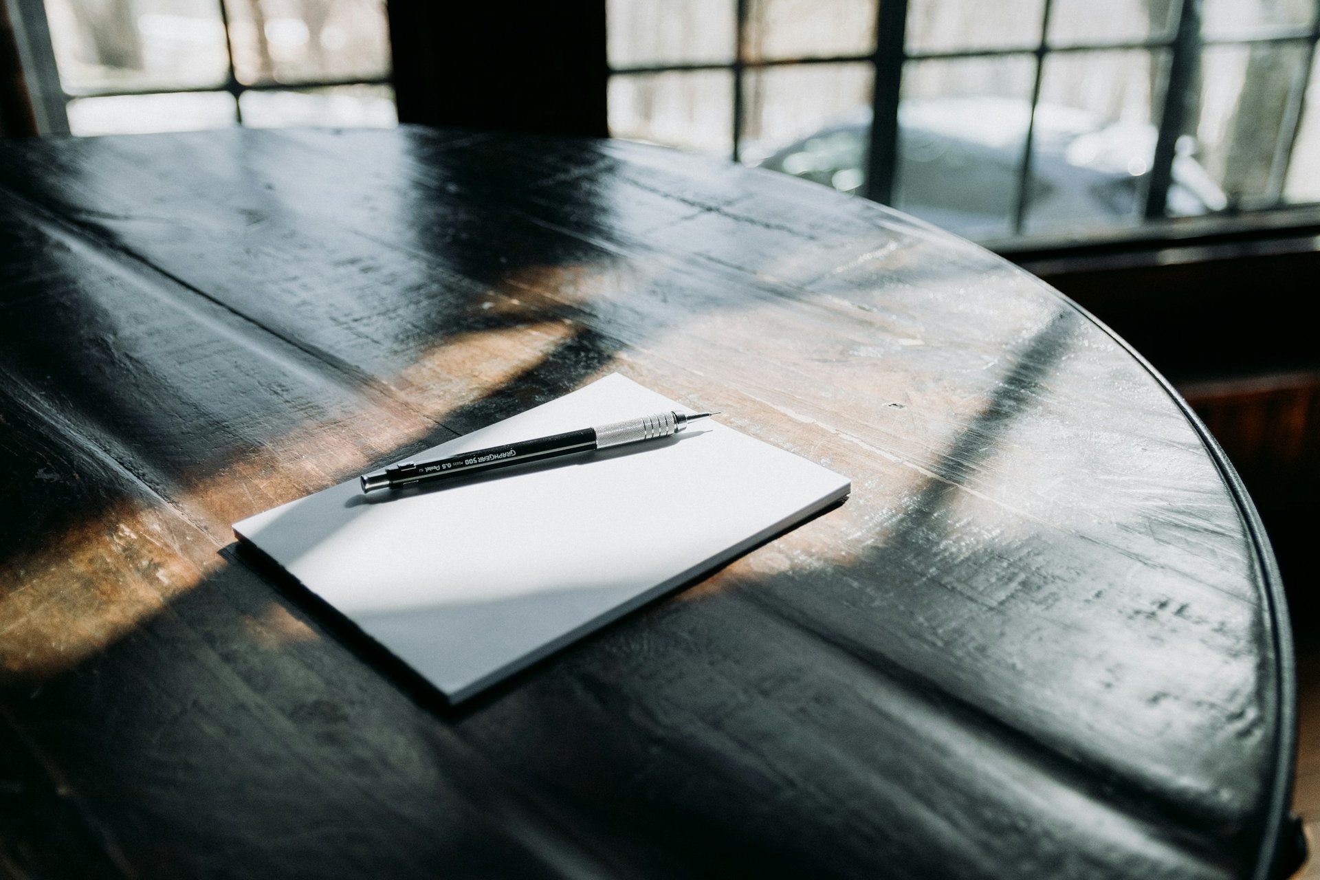Dark wood table with a pen and notepad in an office, in front of windows