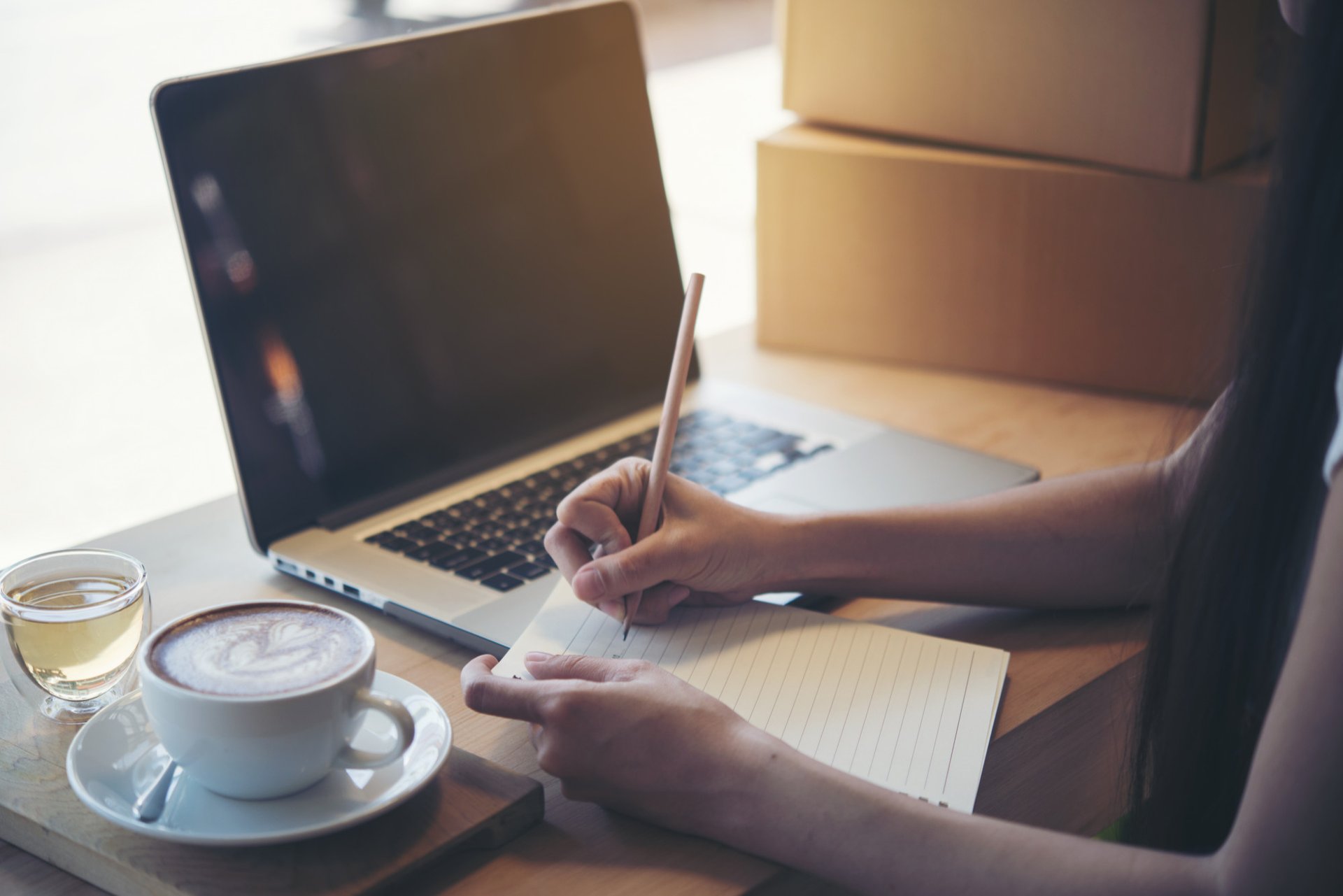 A smartphone on a laptop with coffee, notebook, and pen.