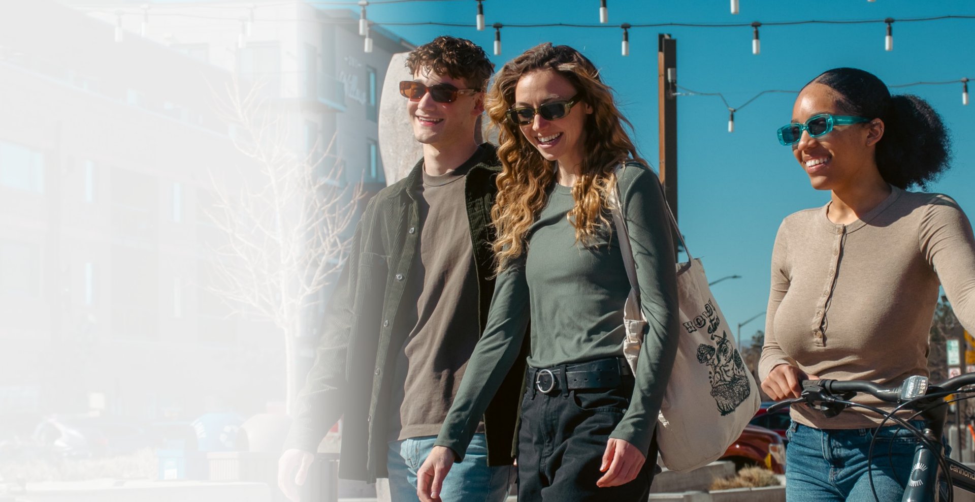 Young man and two women walking and smiling wearing sunglasses.