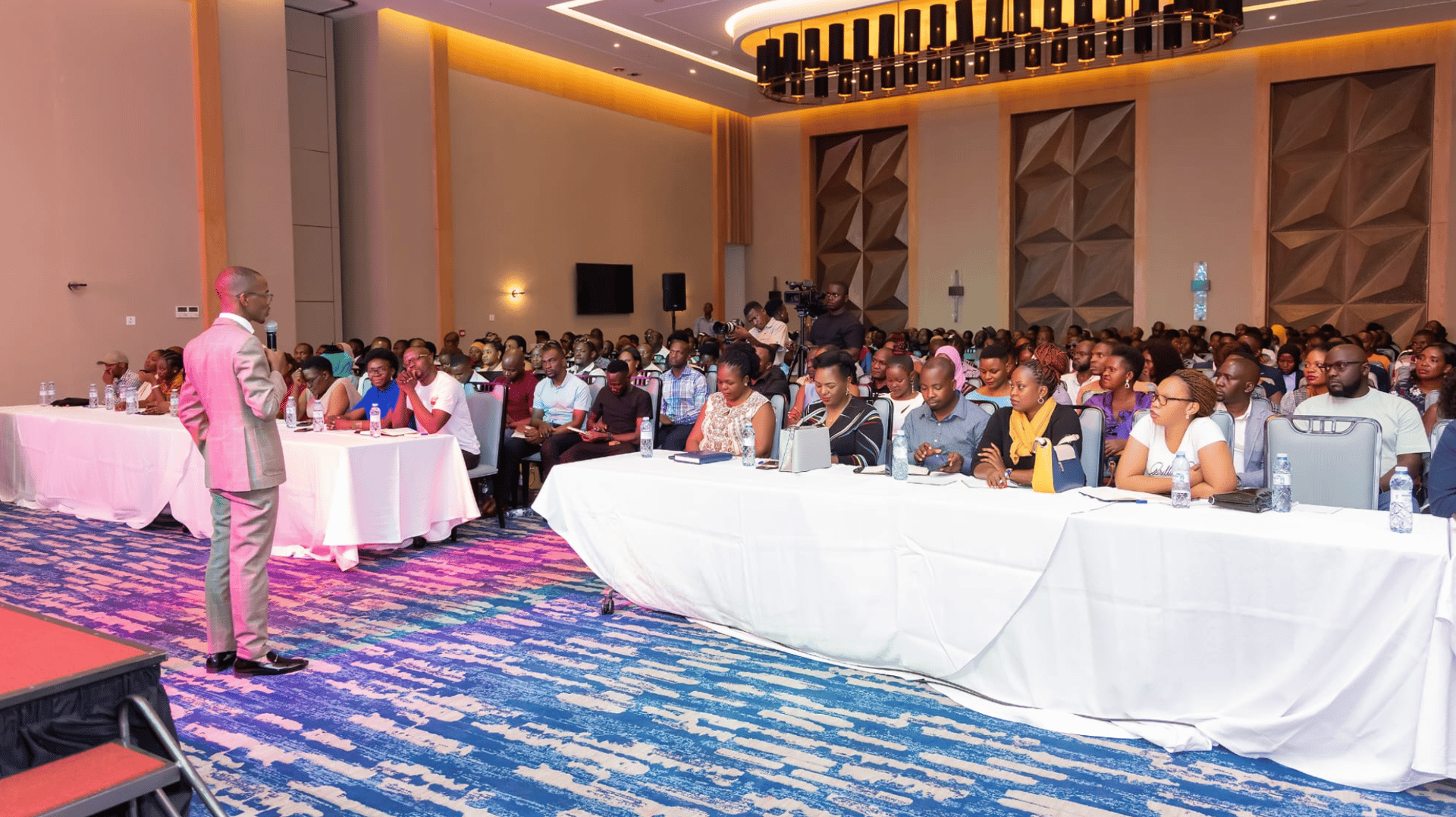 Teacher pointing at students with raised hands in lecture hall.