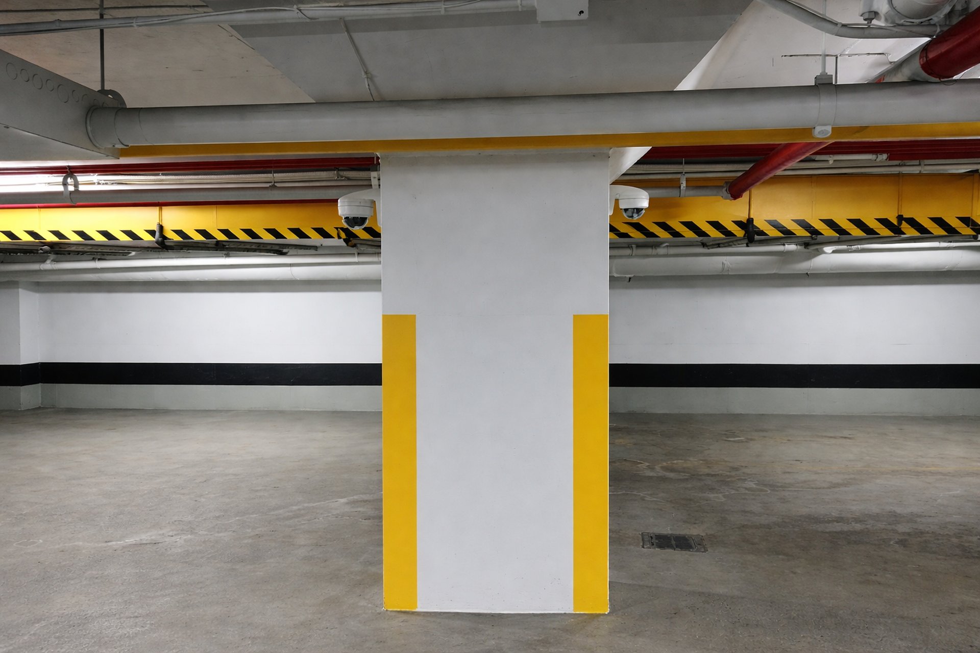 Underground parking garage with central support column exposed pipes and ceiling mounted