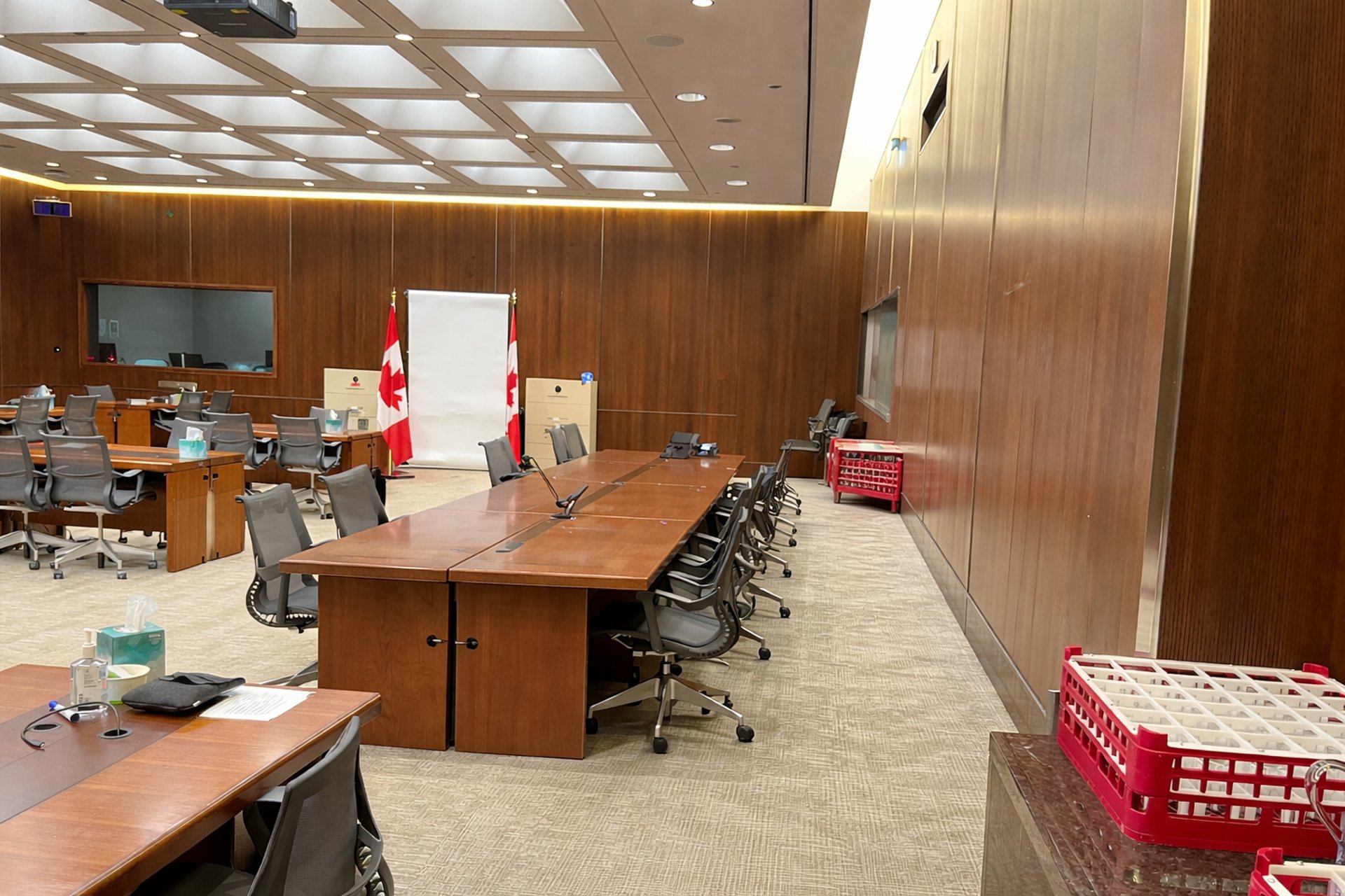 Modern conference room with wood panel walls, meeting tables, chairs, and Canadian flags.