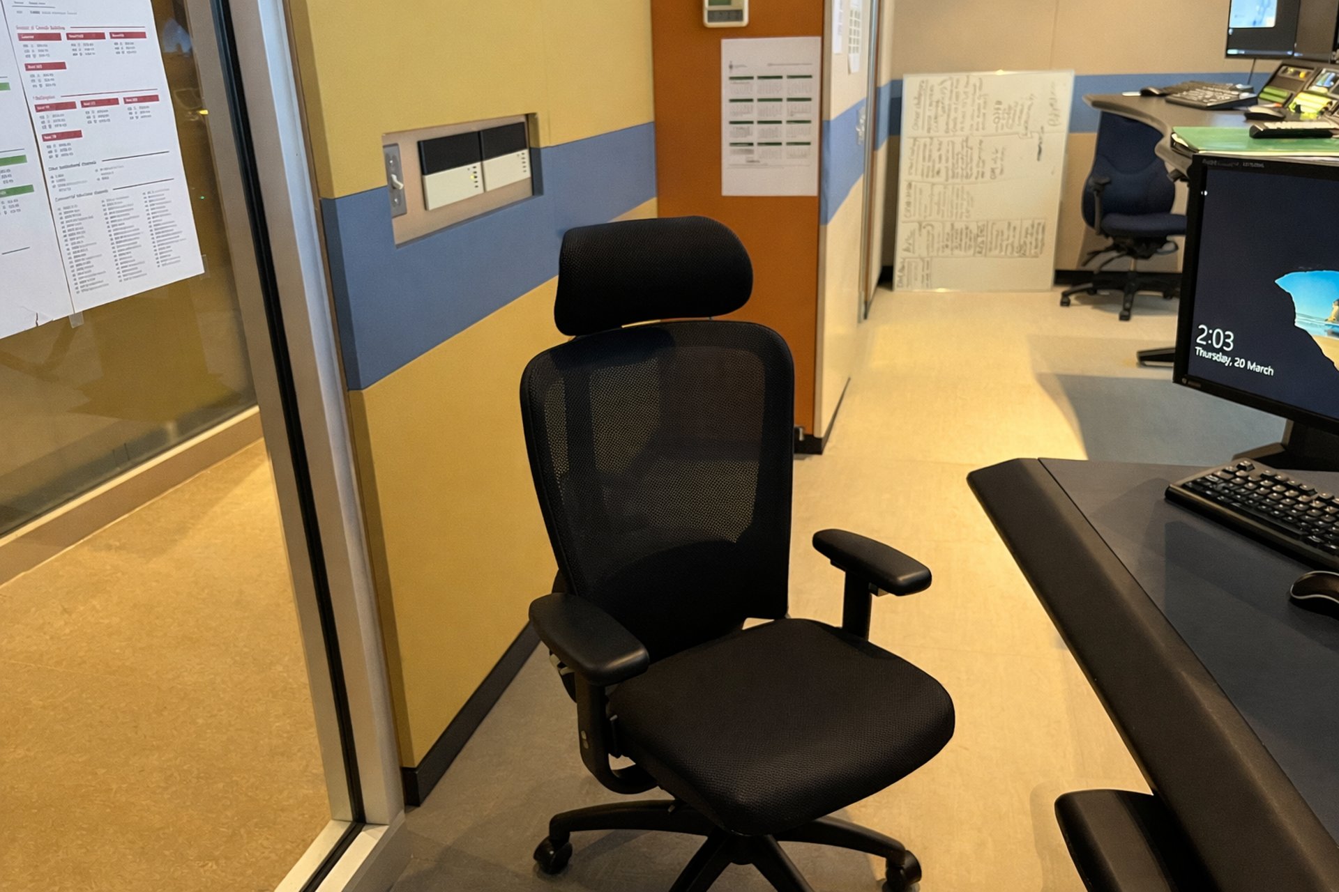 Security operations desk with monitor, keyboard, and chair beside glass control room wall.