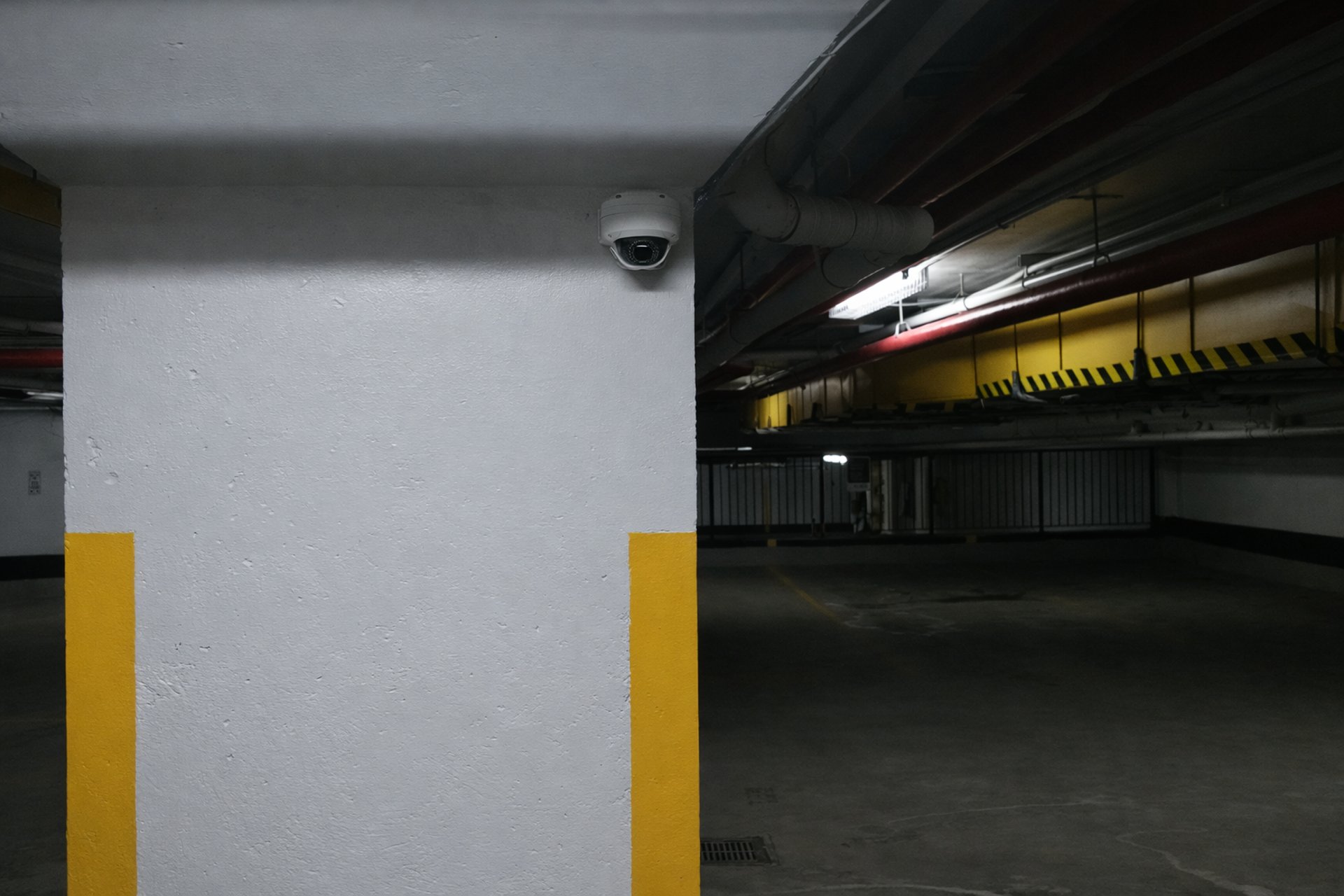 Underground parking garage with concrete column, ceiling pipes, and dome security camera.
