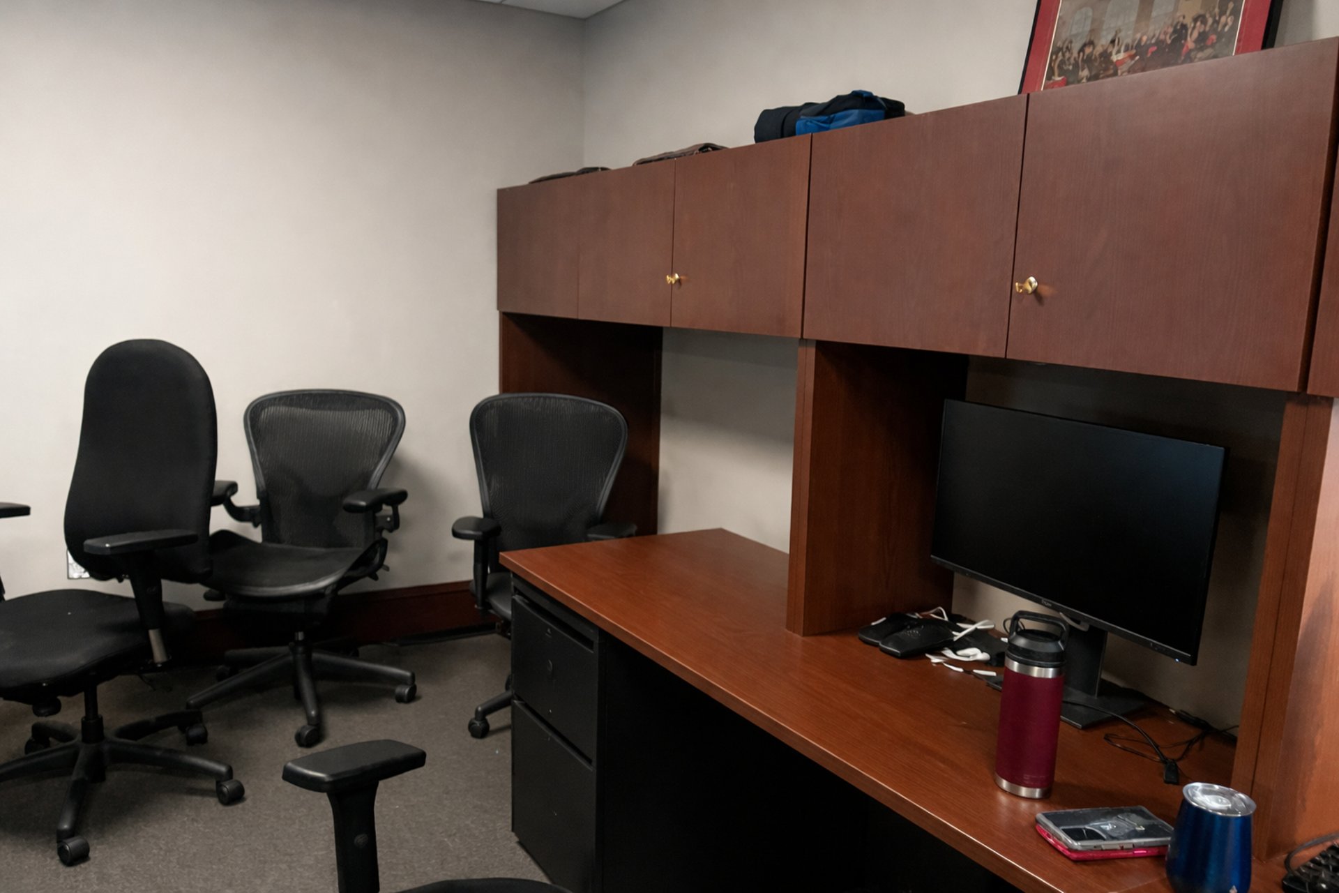 Office workspace with desk, computer monitor, chairs, and storage cabinets.