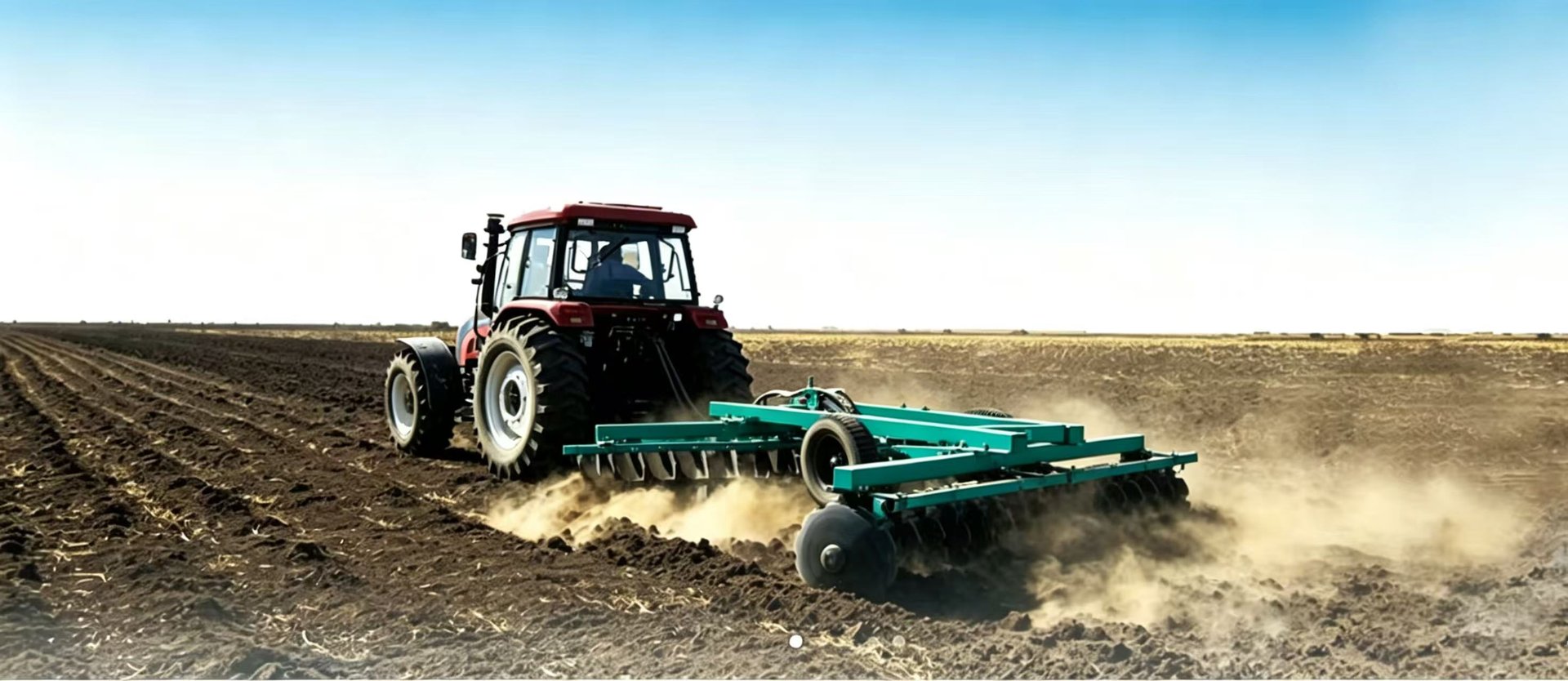 Green tractor plowing a brown field under a cloudy sky