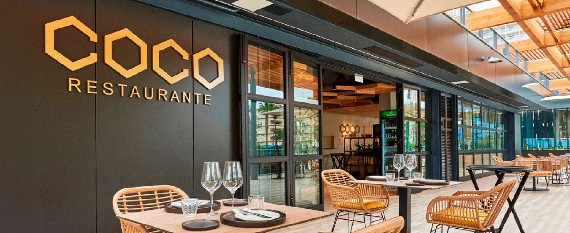 Exterior luminoso del restaurante Coco con su cartel principal y mobiliario