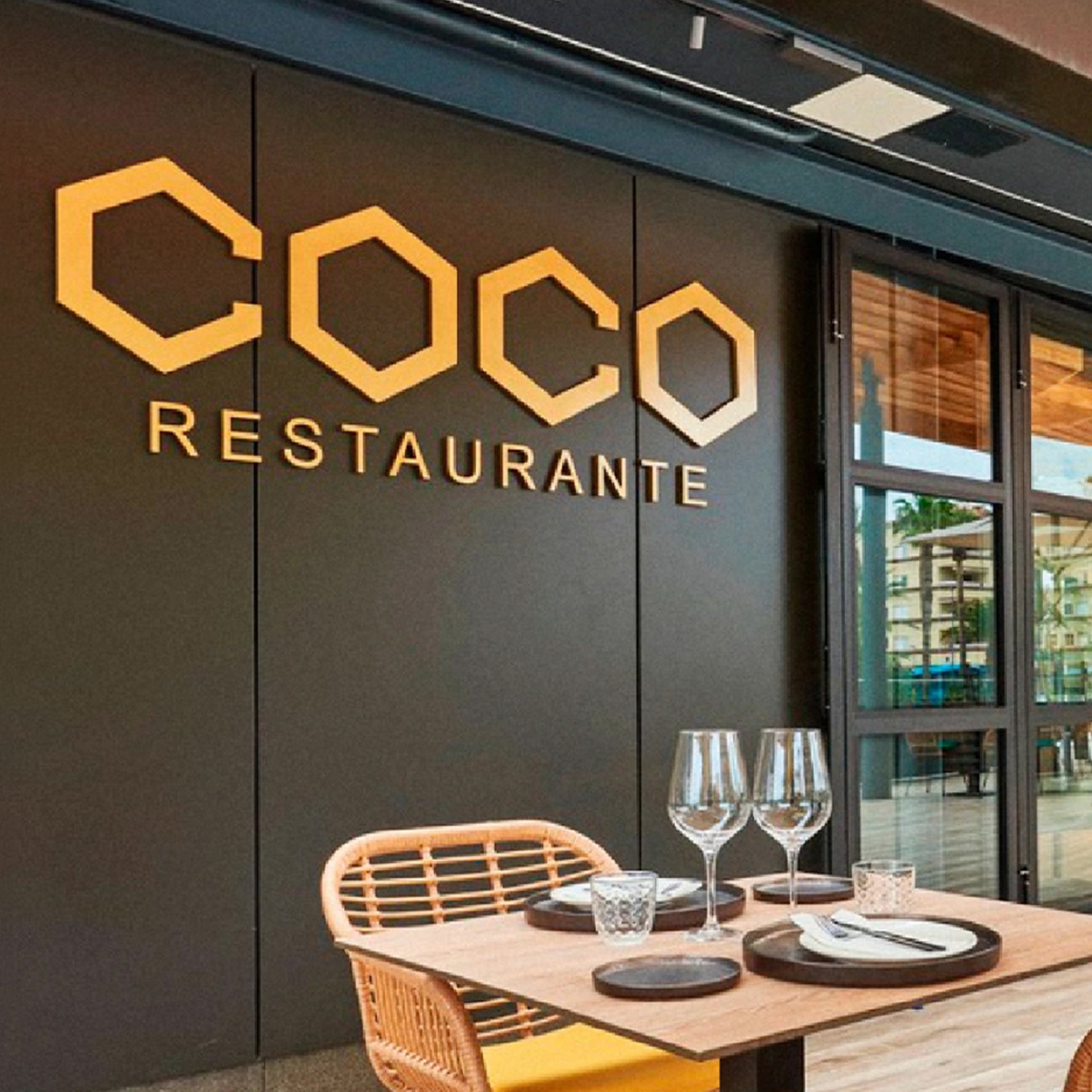 Exterior luminoso del restaurante Coco con su cartel principal y mobiliario