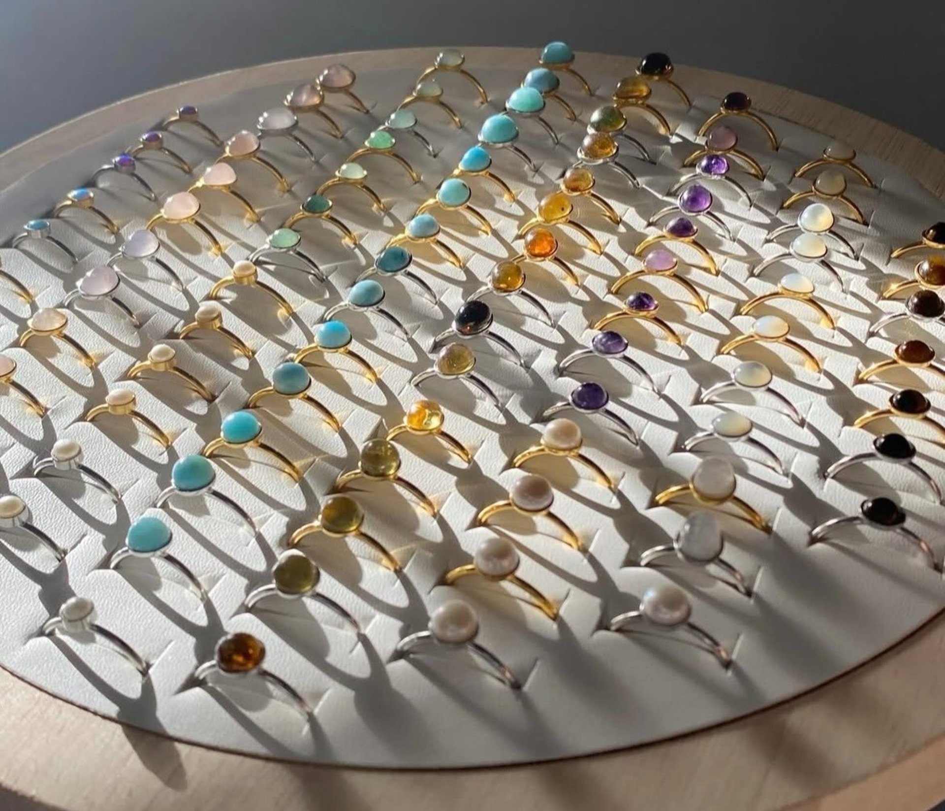 Anillos dorados con diferentes tipos de piedras preciosas sobre un exhibidor de madre y tela blanca. 