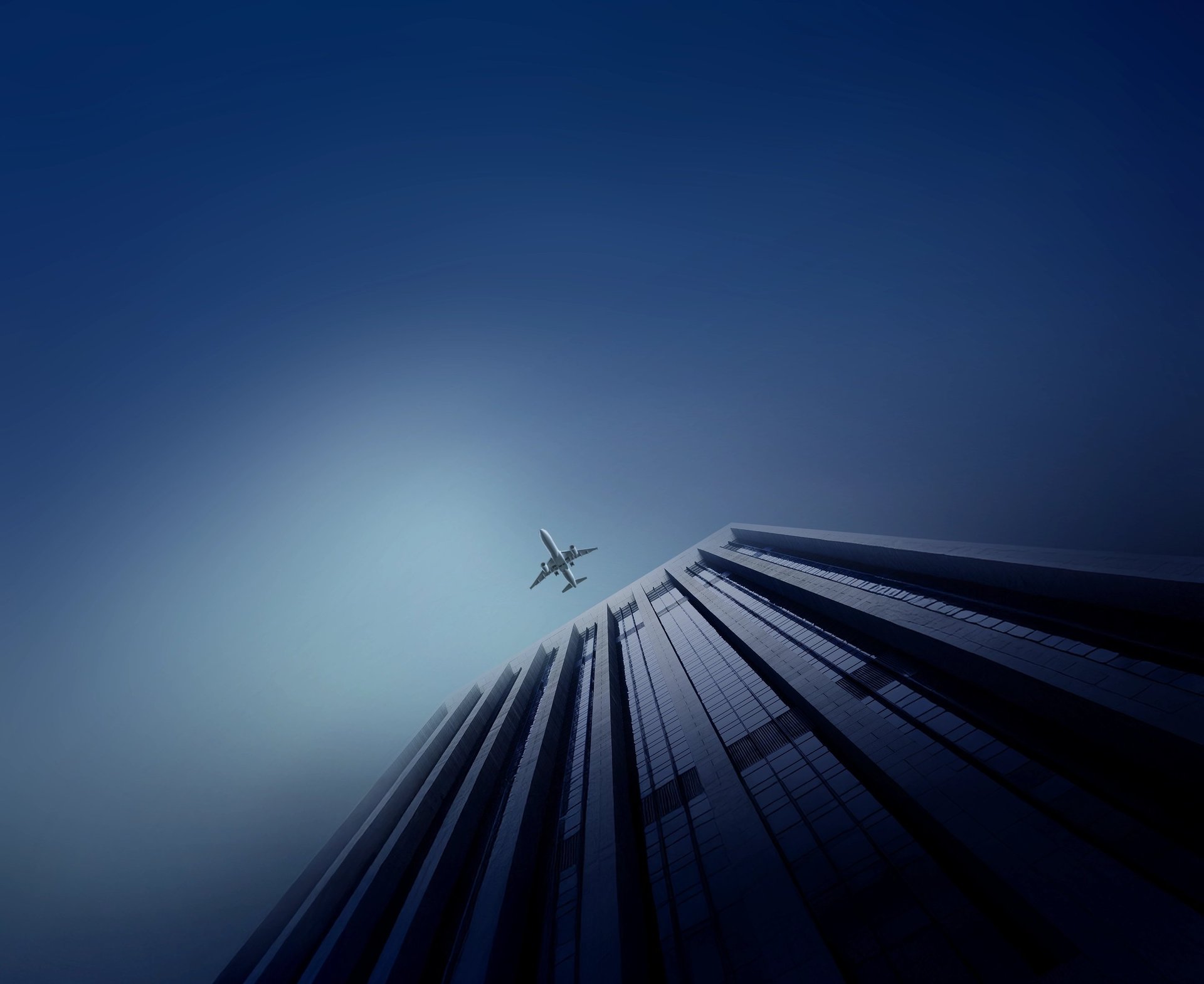bottom view shot of airplane flying above high rise building