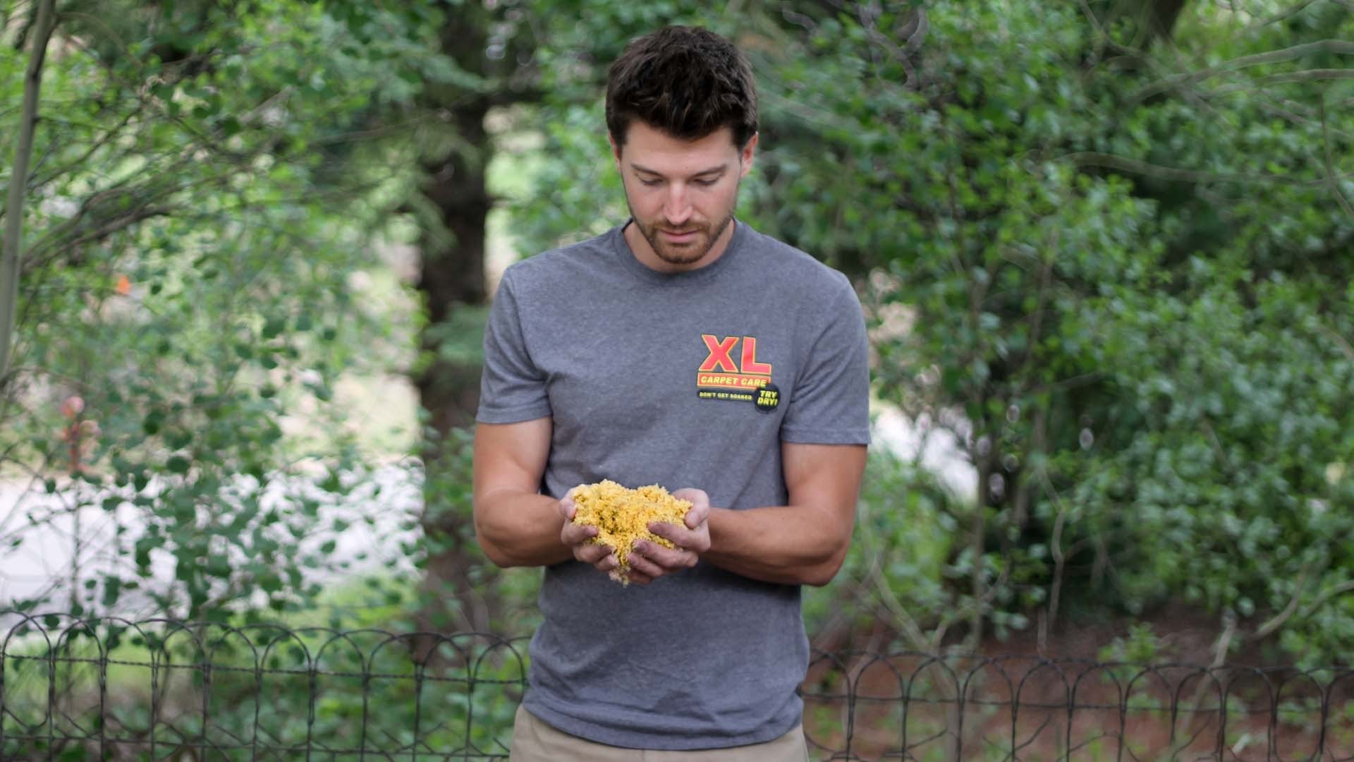 Man holding handful of XL dry extraction carpet sponges. XL Carpet Care logo on shirt.