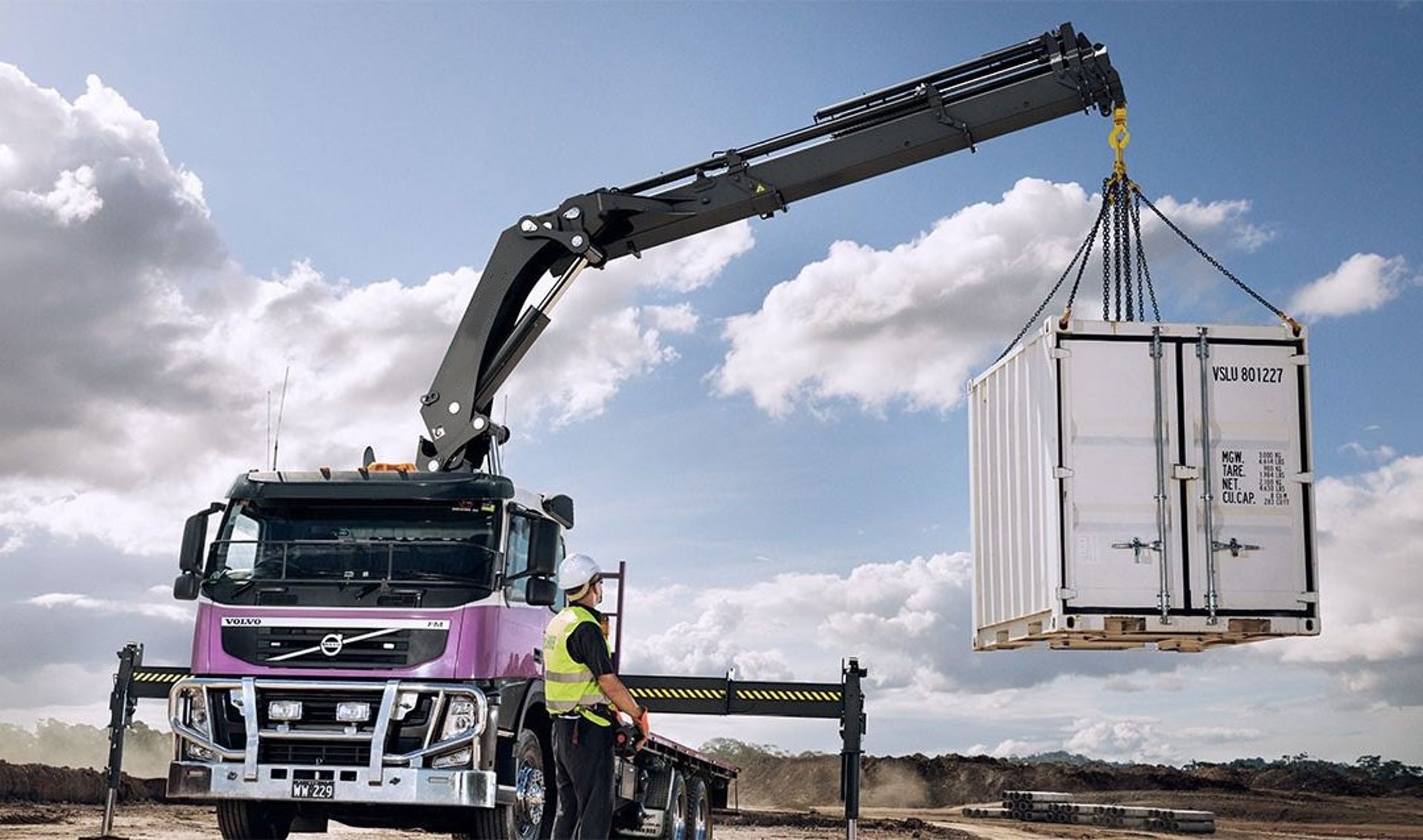 A knuckle boom crane with RC lifting a container onto a truck.