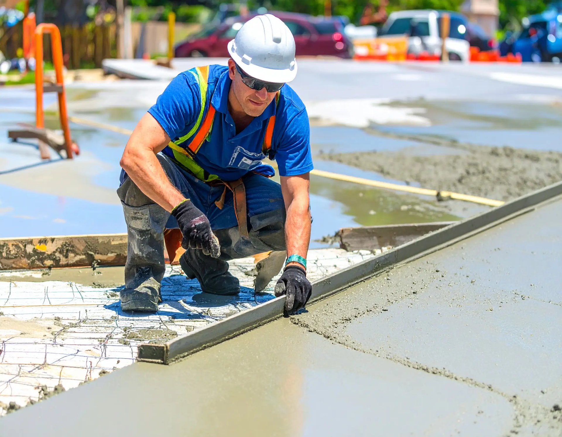 Man in safety hard hat leveling a fresh concrete sidewalk