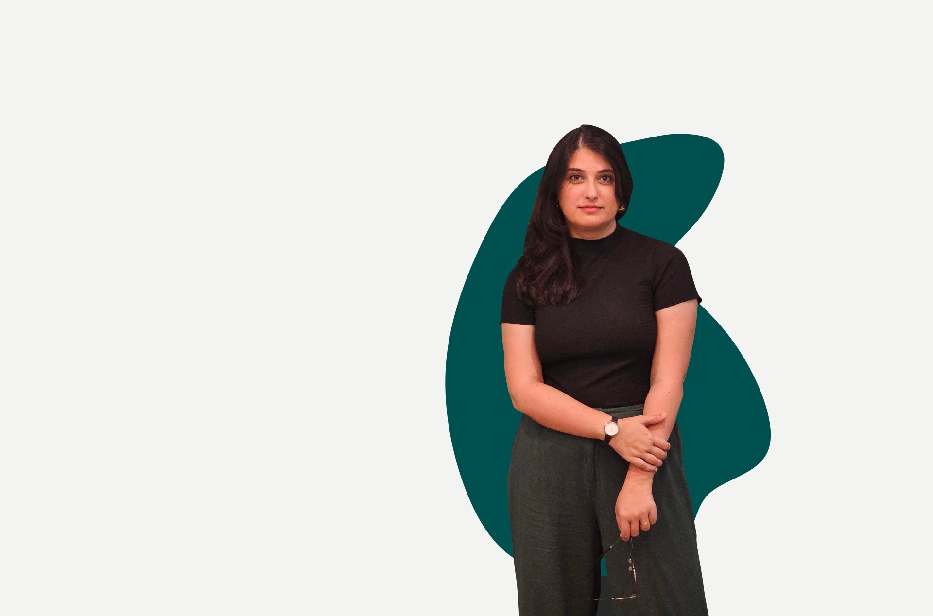 Pessoa de braços cruzados, segurando óculos, usando blusa preta de manga curta, em frente a formas abstratas verdes.