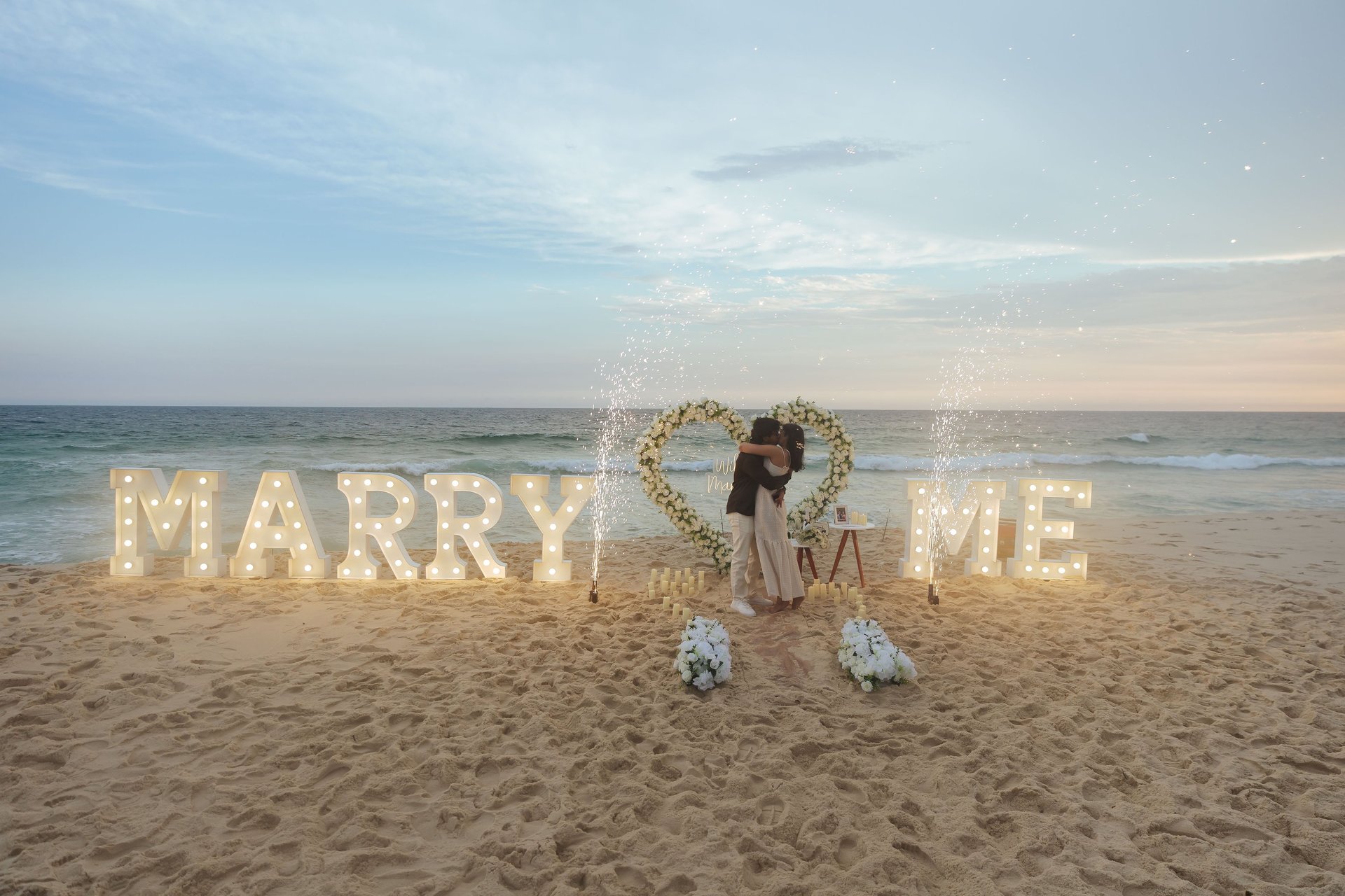man kneeling in front of woman on rock at beach