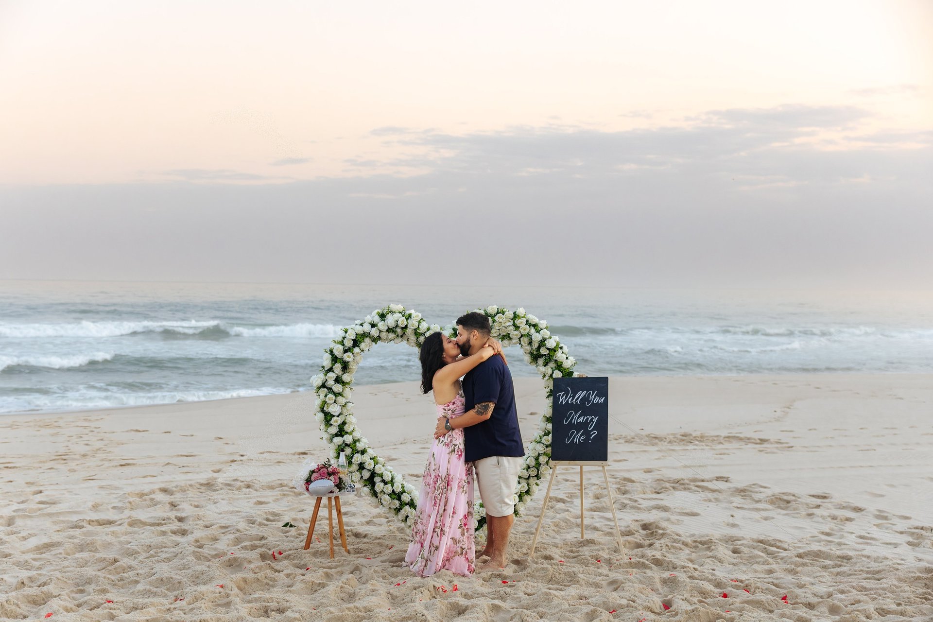 man kneeling in front of woman on rock at beach