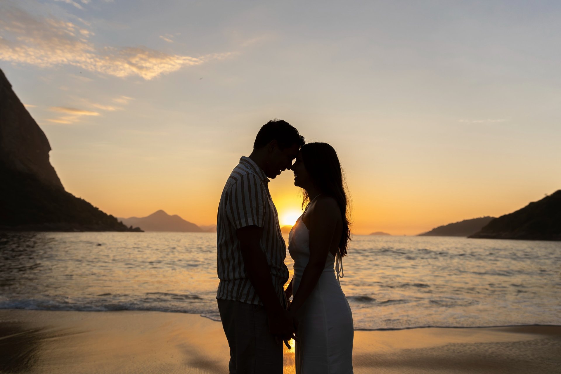 man kneeling in front of woman on rock at beach