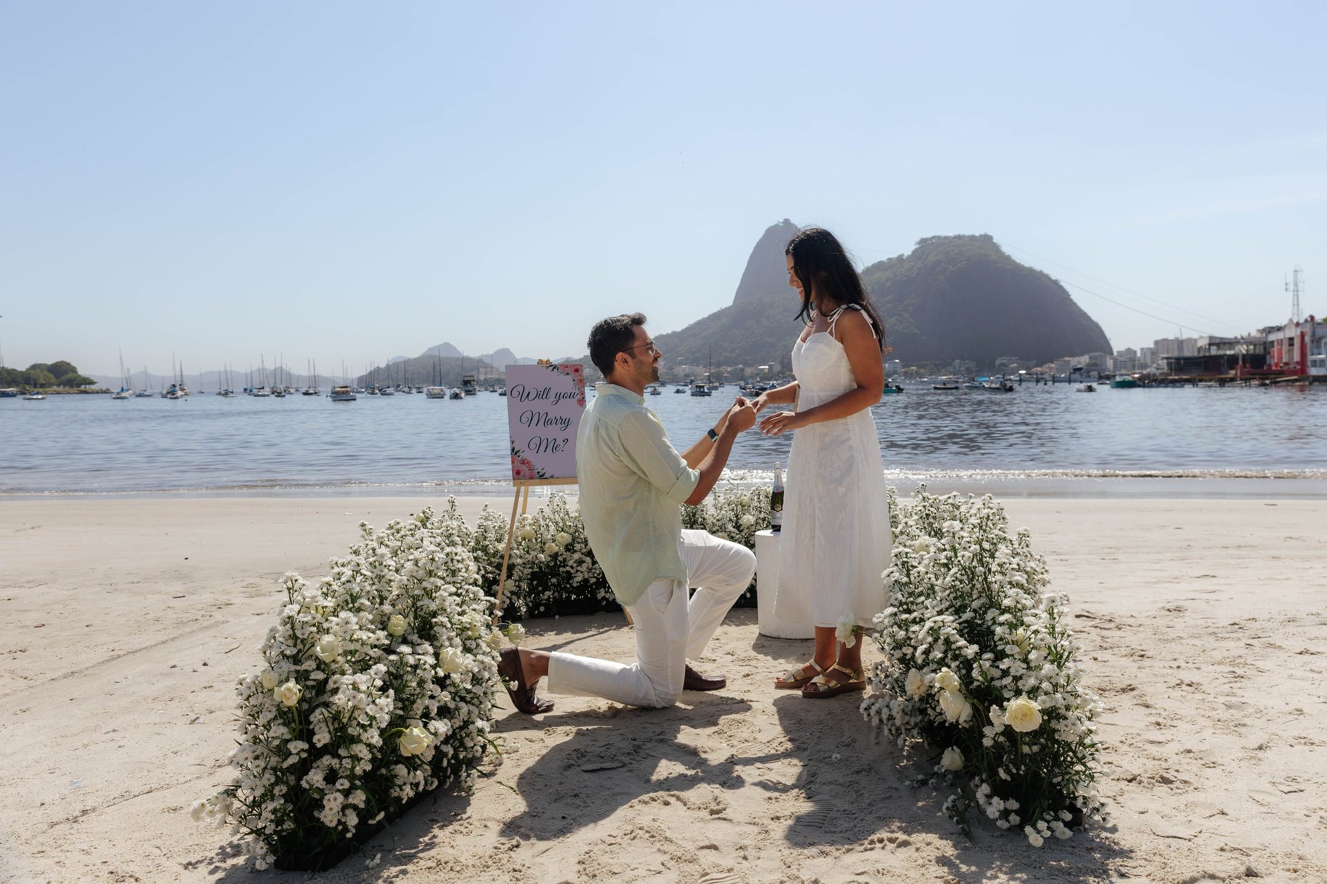 man kneeling in front of woman on rock at beach