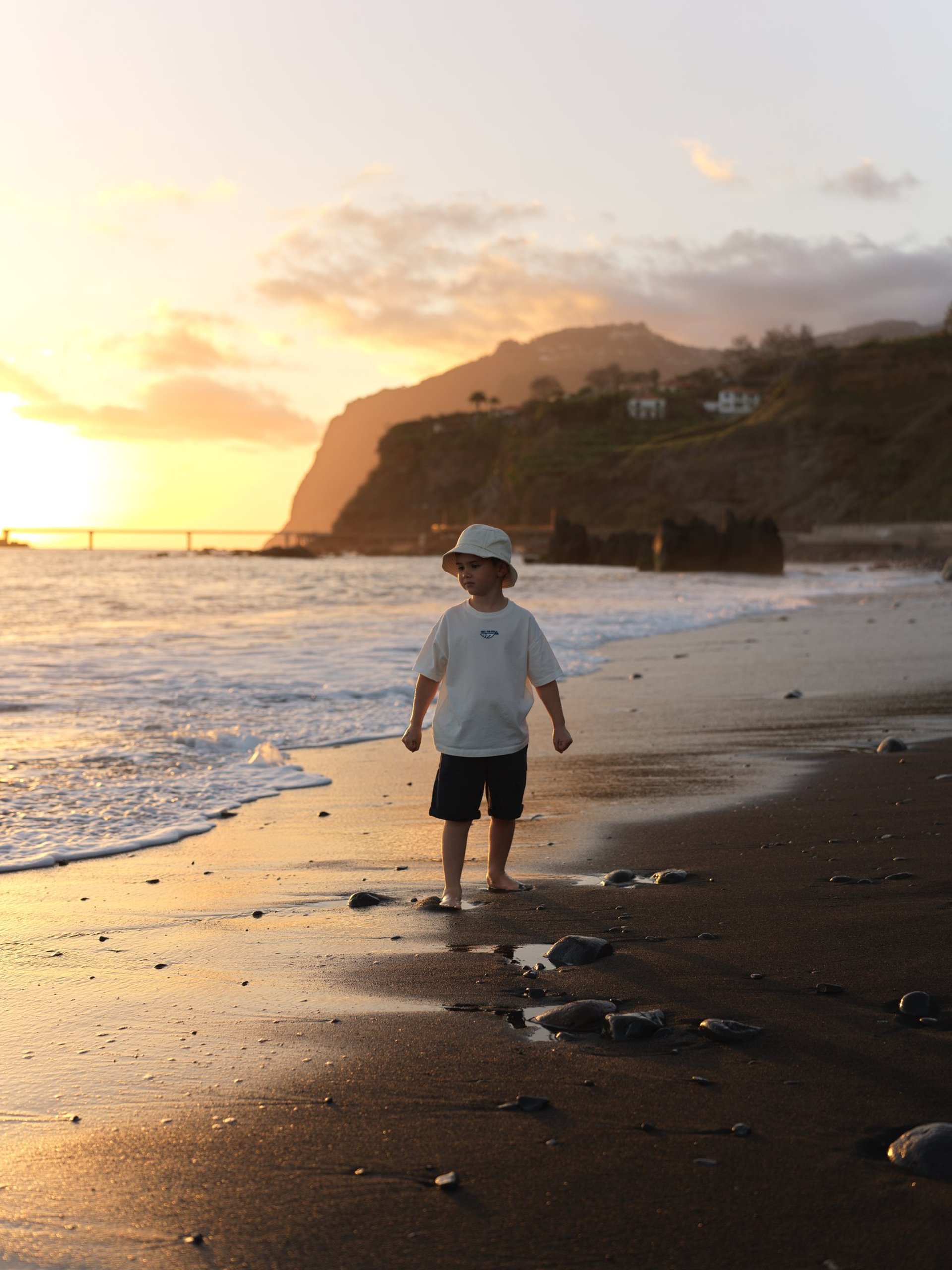 Child walks barefoot on Madeira beach at sunset, Atlantic waves and golden cliffs create a natural lifestyle vacation mood.