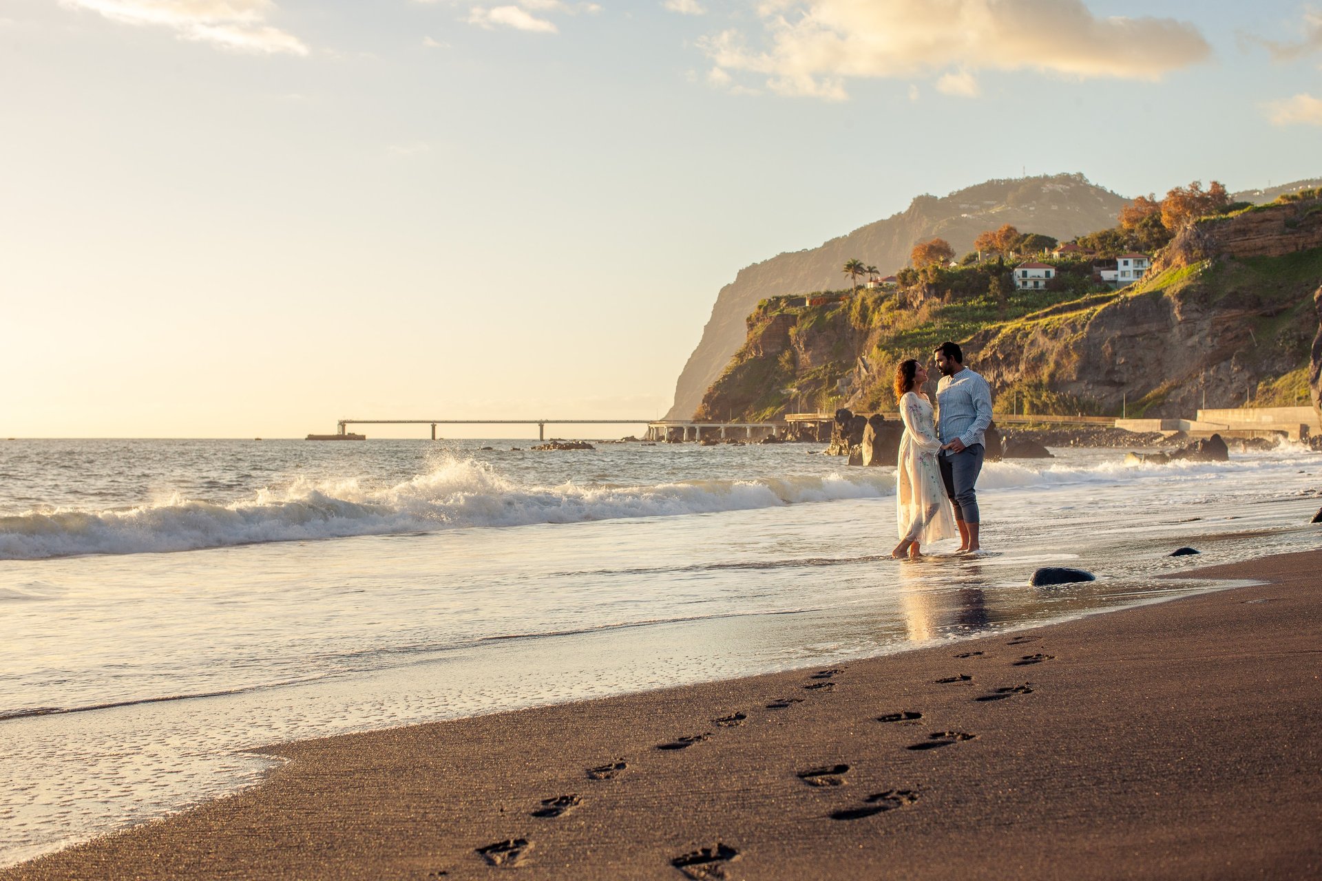 Romantic couple in waves on Praia Formosa black sand beach, Madeira, sunset cliffs view