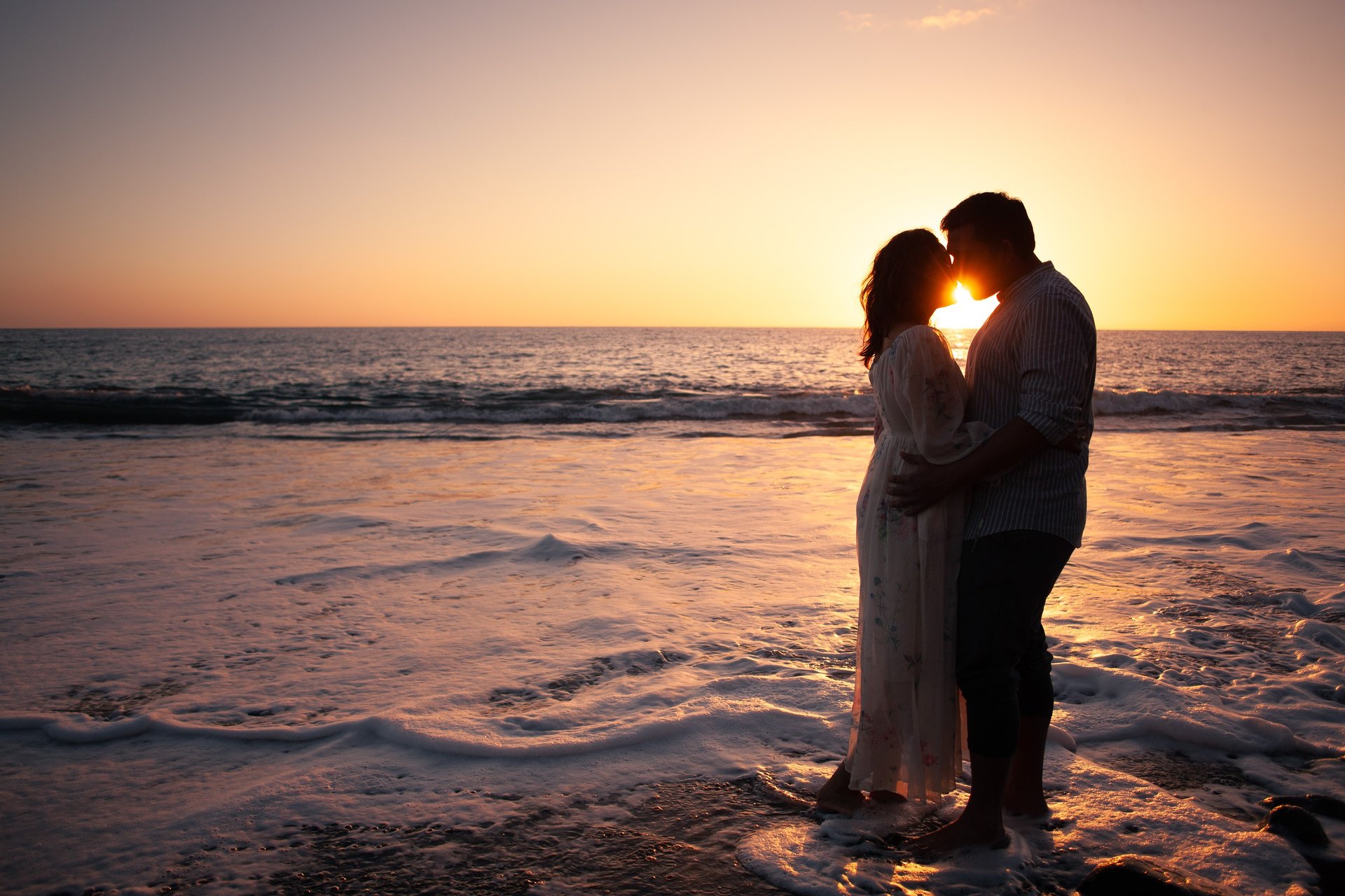 Happy couple kissing silhouette at sunset on Praia Formosa beach, Madeira, ocean waves, romantic coastal portrait.