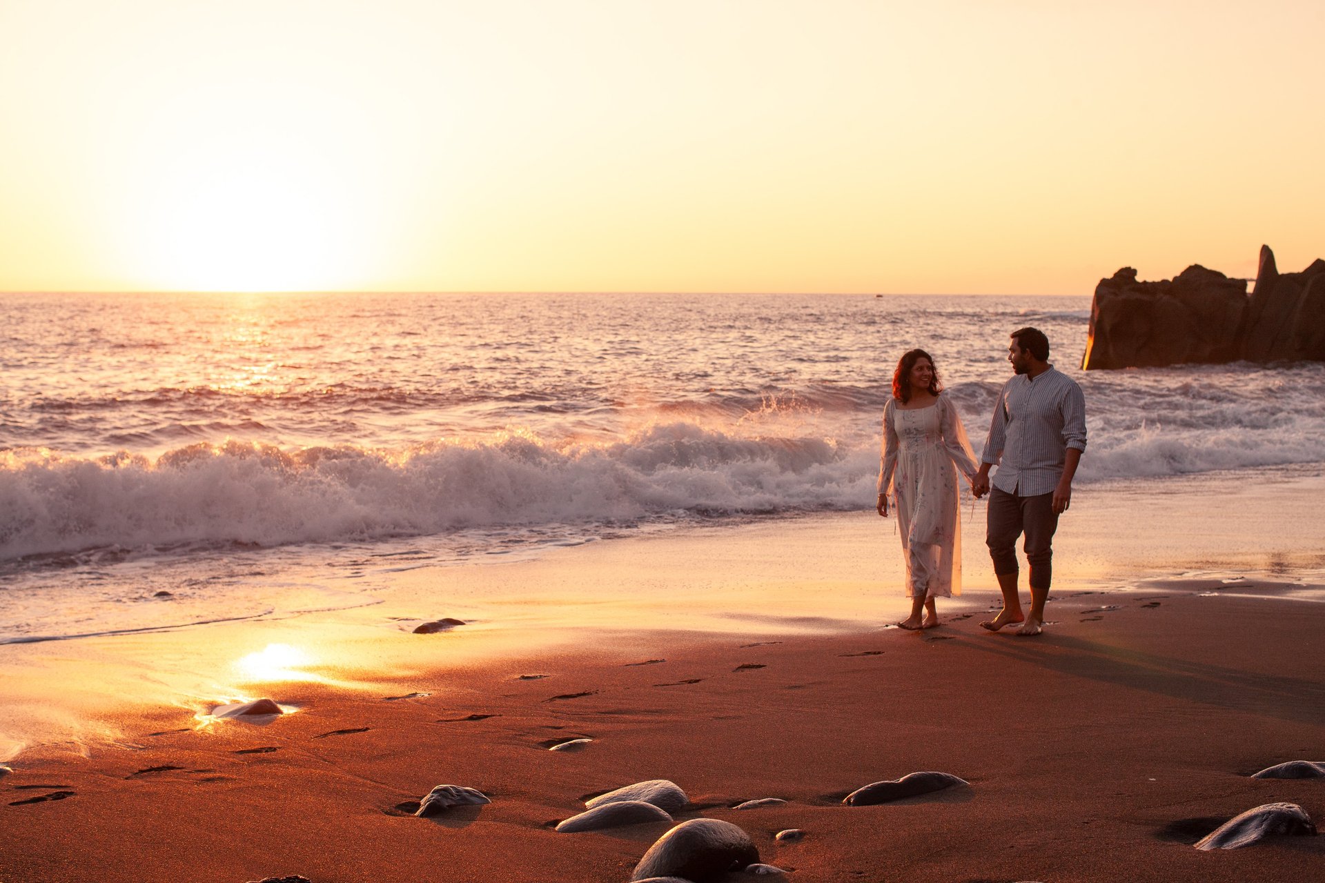 Happy couple holding hands at sunset on Praia Formosa black-sand beach, Madeira, ocean waves