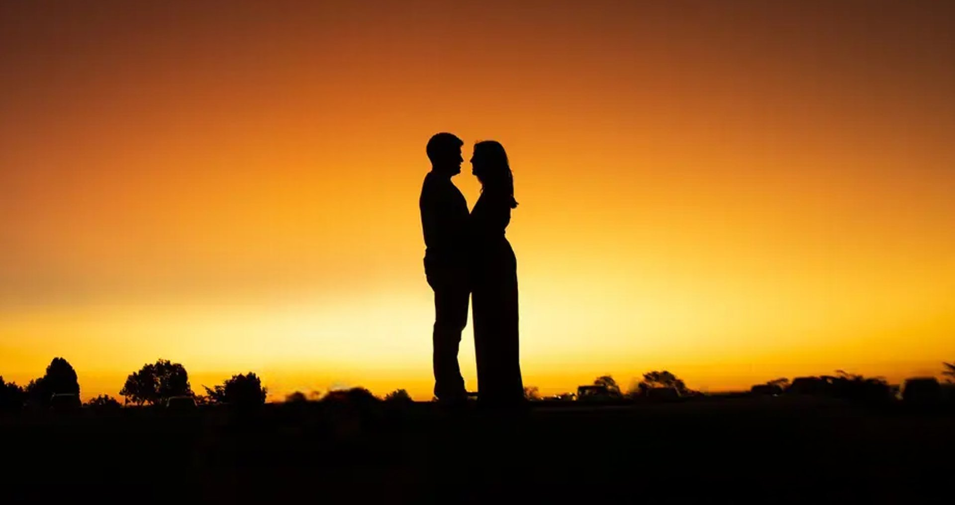 silhouette of man and woman standing beside cross during sunset