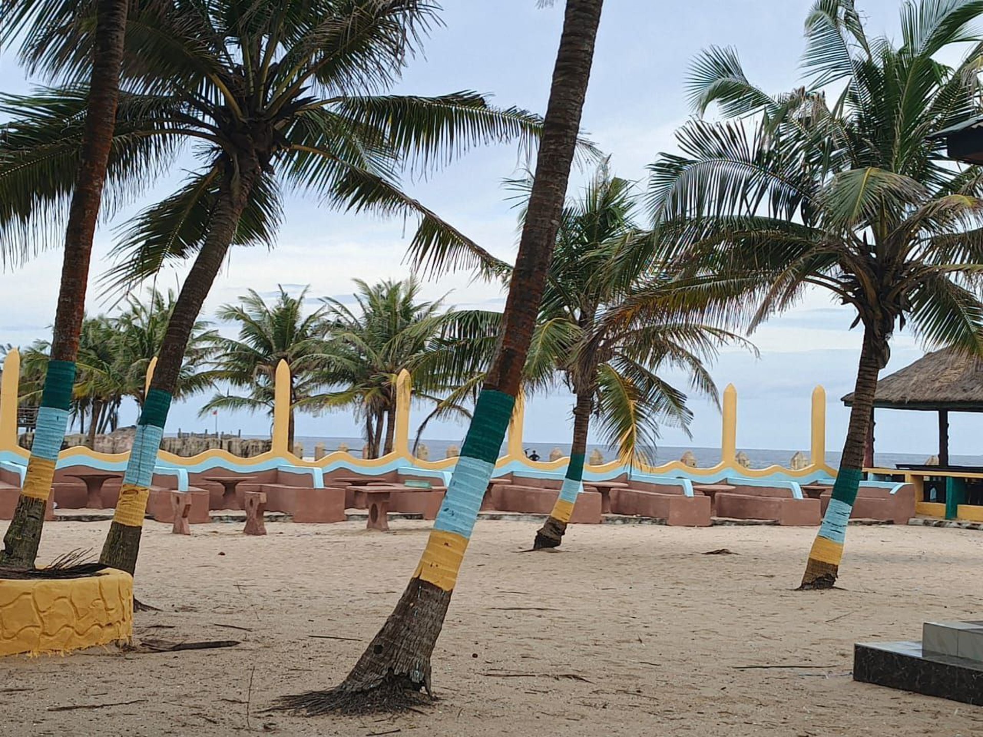 brown nipa hut near palm trees and body of water during daytime
