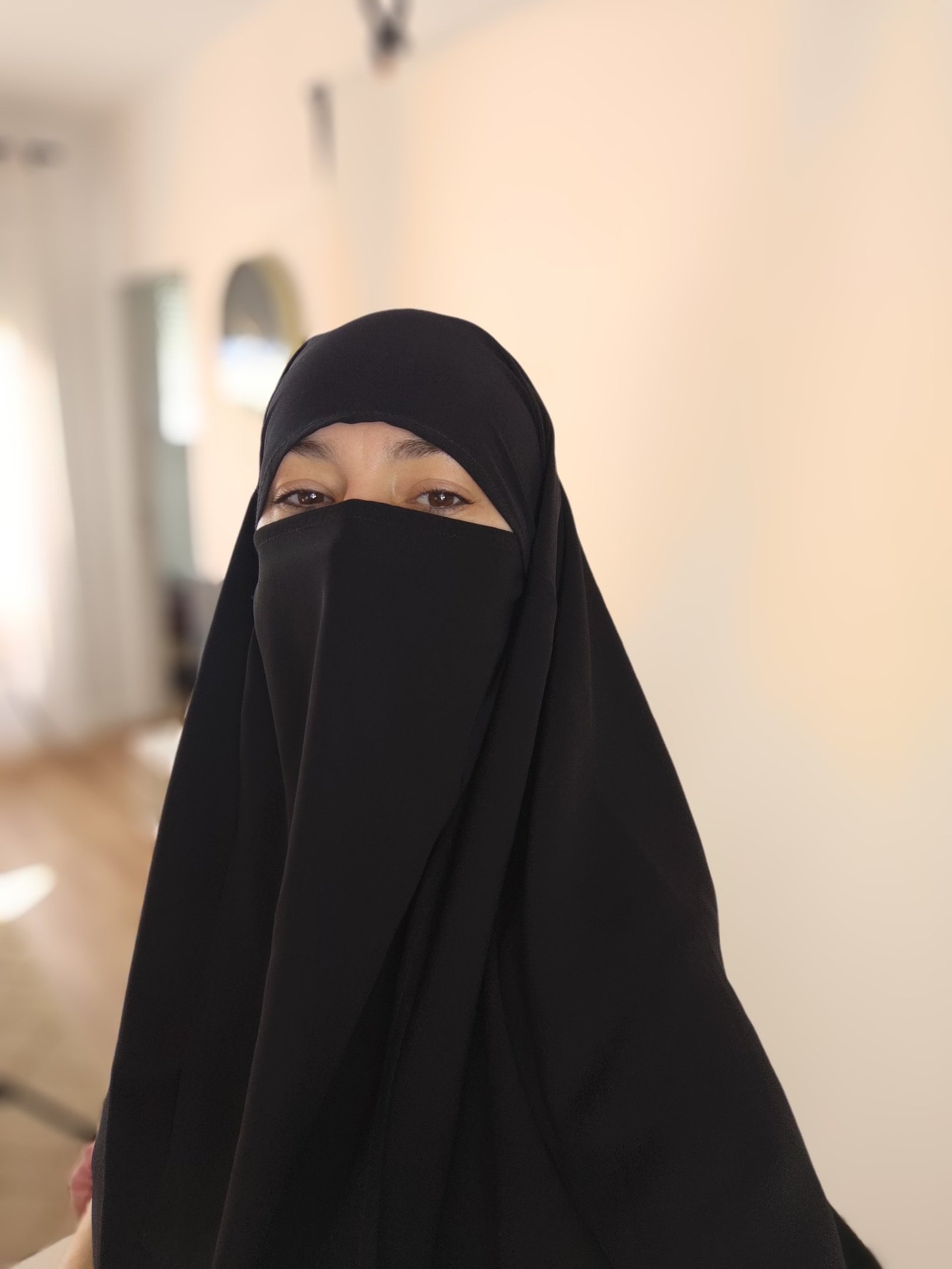 a woman in a black hijab is standing in front of a white building