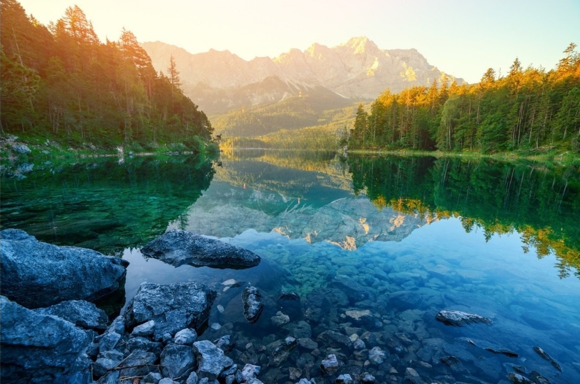 Vue sur un lac de montagne entouré de forêts et de sommets éclairés par le soleil