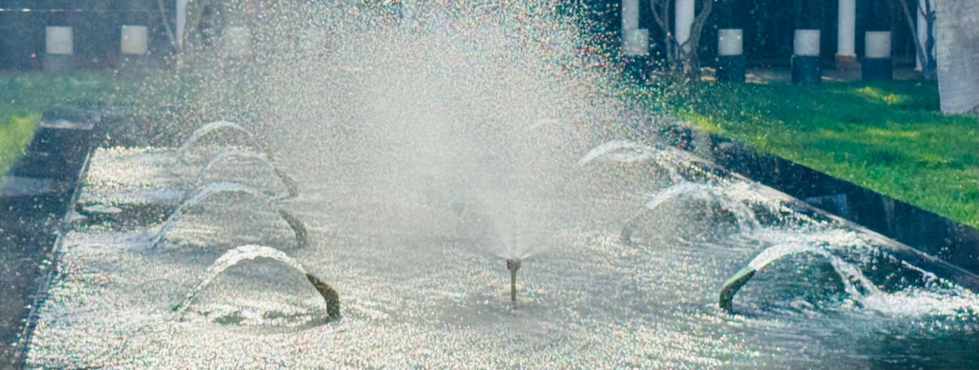 Photo showing multiple flowing water fountains with thousands of water droplets catching the sunlight with rainbow effect
