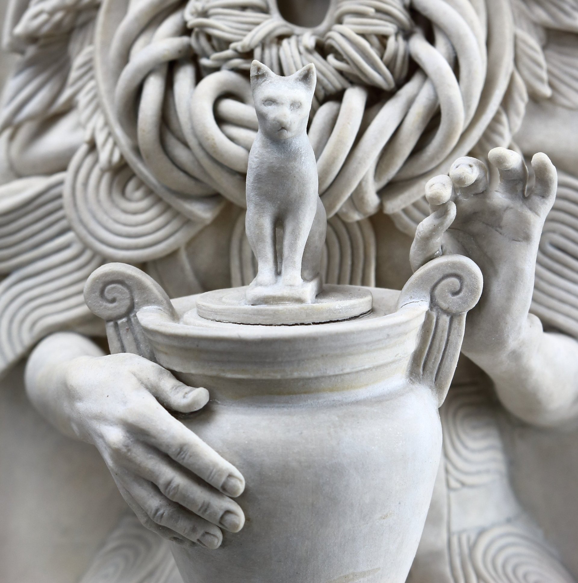 Detail of hands: ceramic sculpture of woman in elaborate dress holding urn with Egyptian cat. 