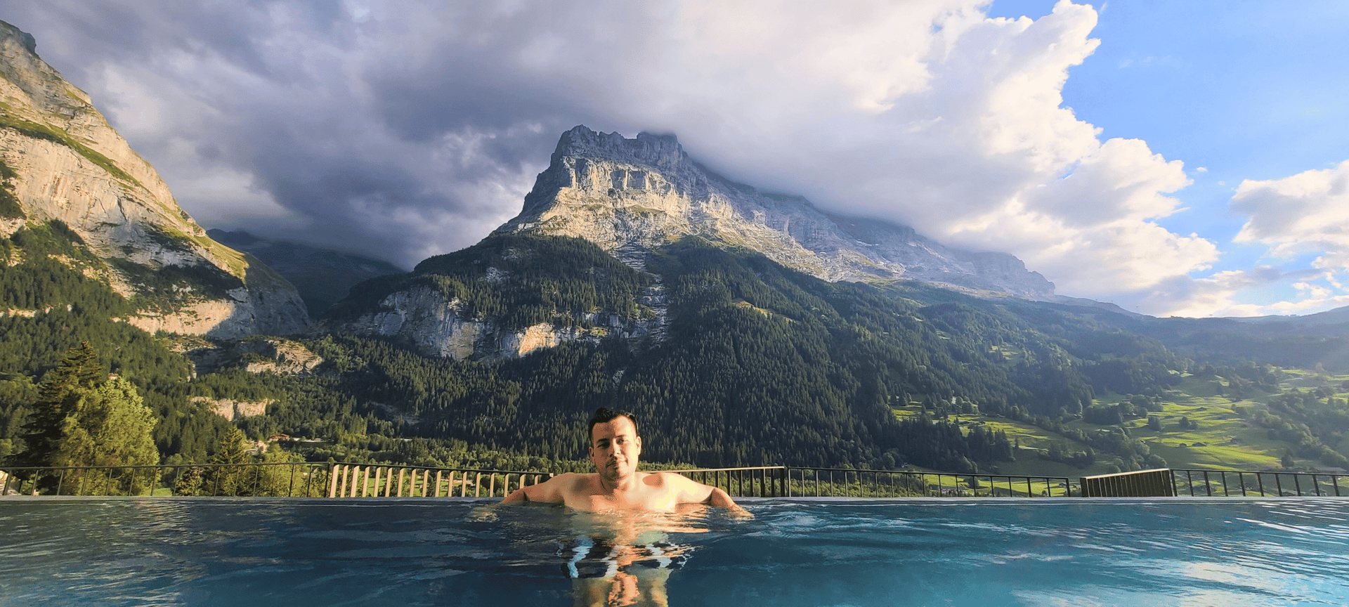 Grindelwald, Switzerland: A man enjoys an infinity pool experience with breathtaking mountain views under a cloudy sky 