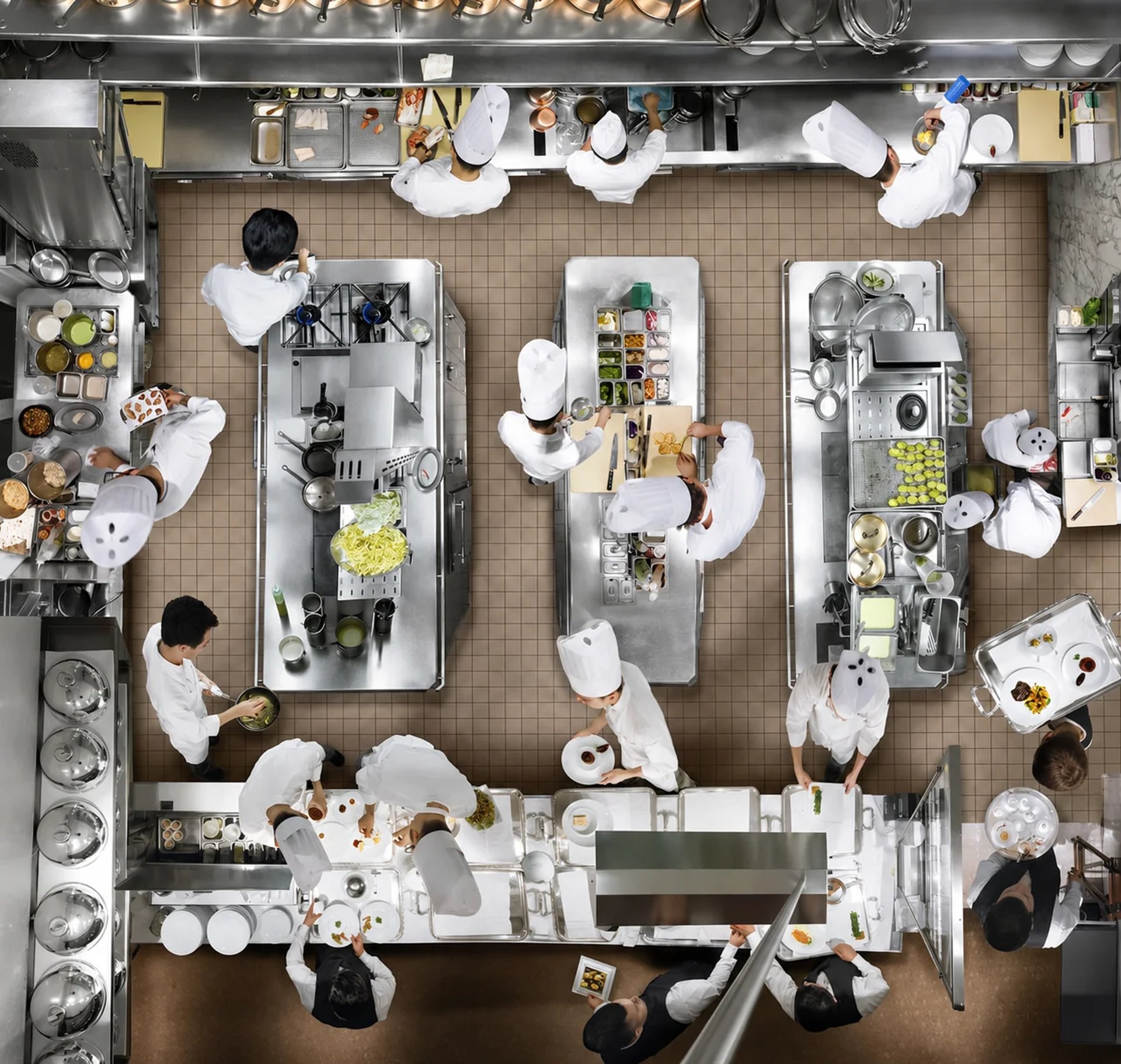 Overhead view of a busy commercial kitchen with chefs working at multiple stainless steel benches.