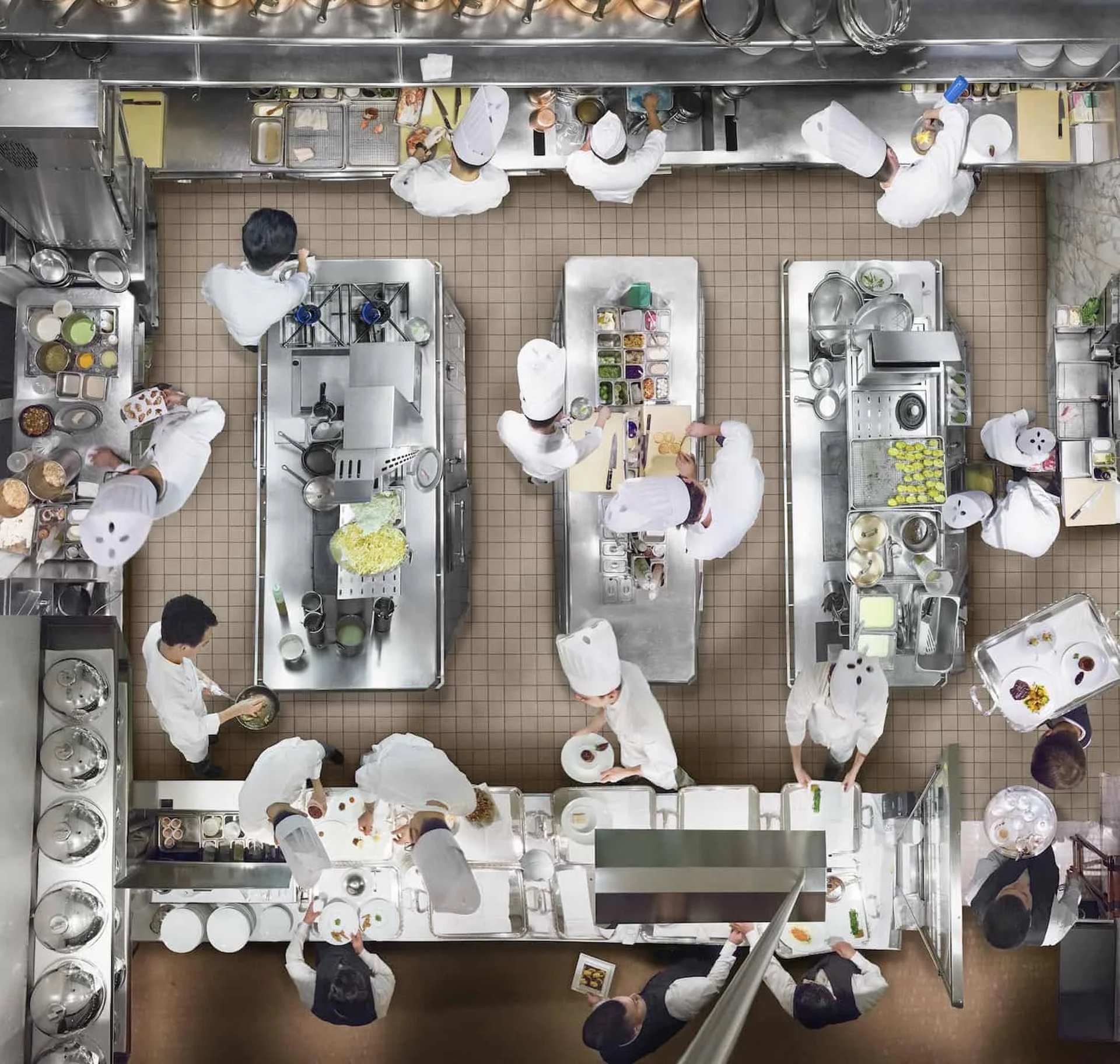 Overhead view of a busy commercial kitchen with chefs working at multiple stainless steel tables.