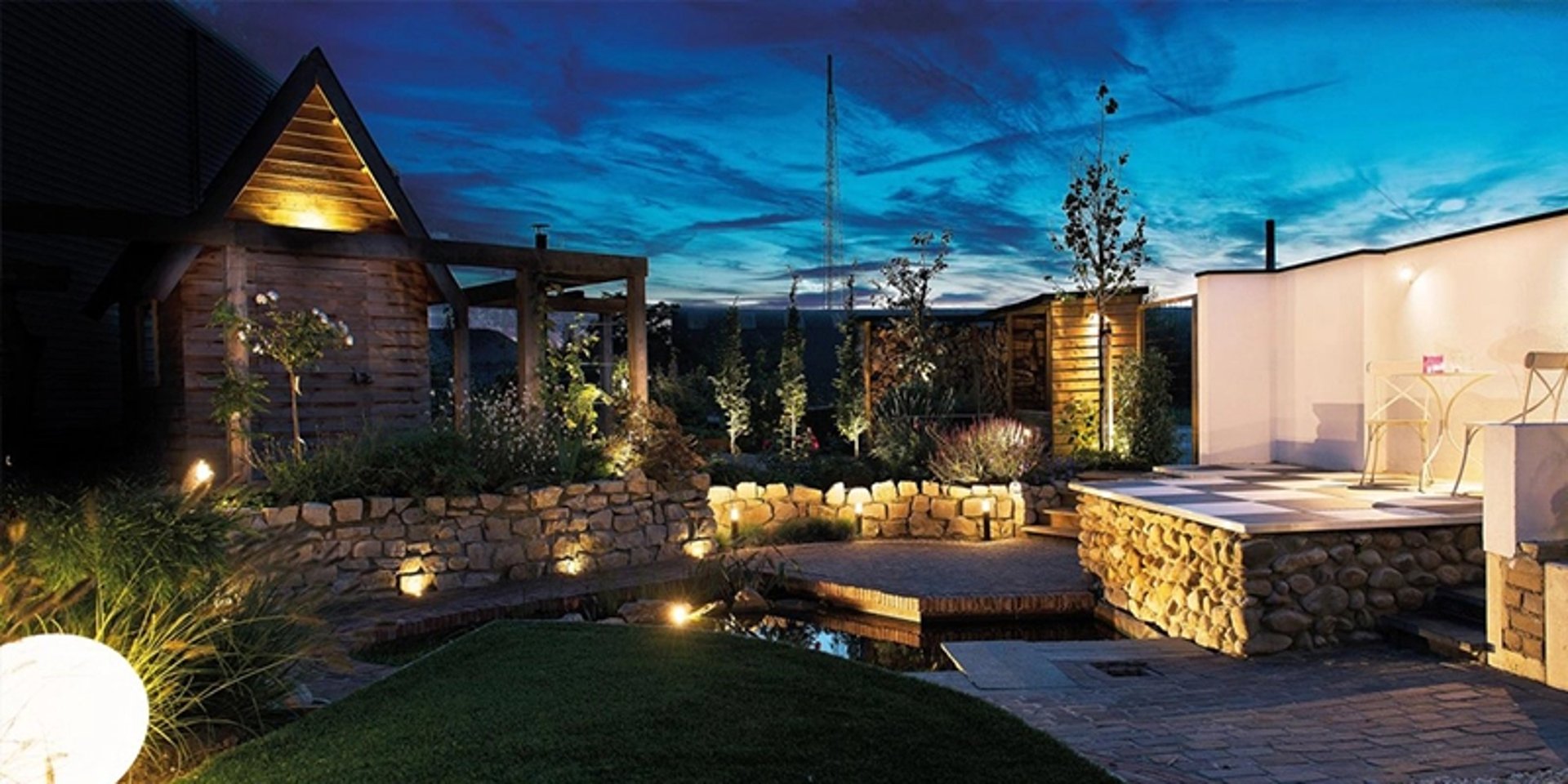 Sfeervolle 12-volt tuinverlichting in een prachtig verlichte achtertuin met vijver, stenen muurtjes en een overkapping