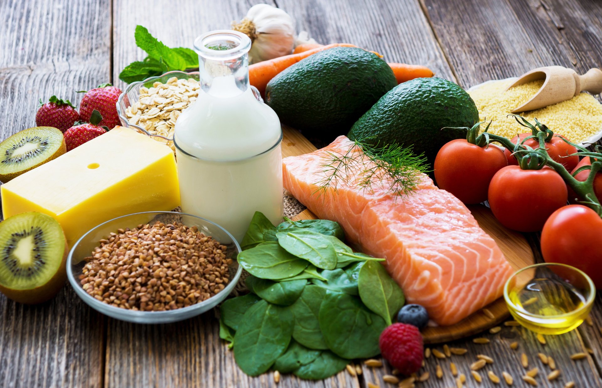 Healthy food assortment with salmon, vegetables, fruits, dairy, grains, and leafy greens on a rustic table, promoting clean e